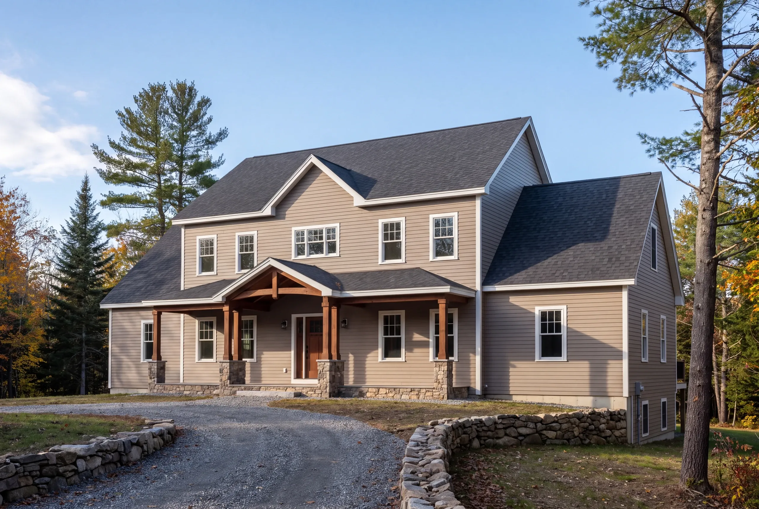 Residential home builder Belfast Maine: taupe two-story house with a timber-post front porch and fieldstone walls along the drive