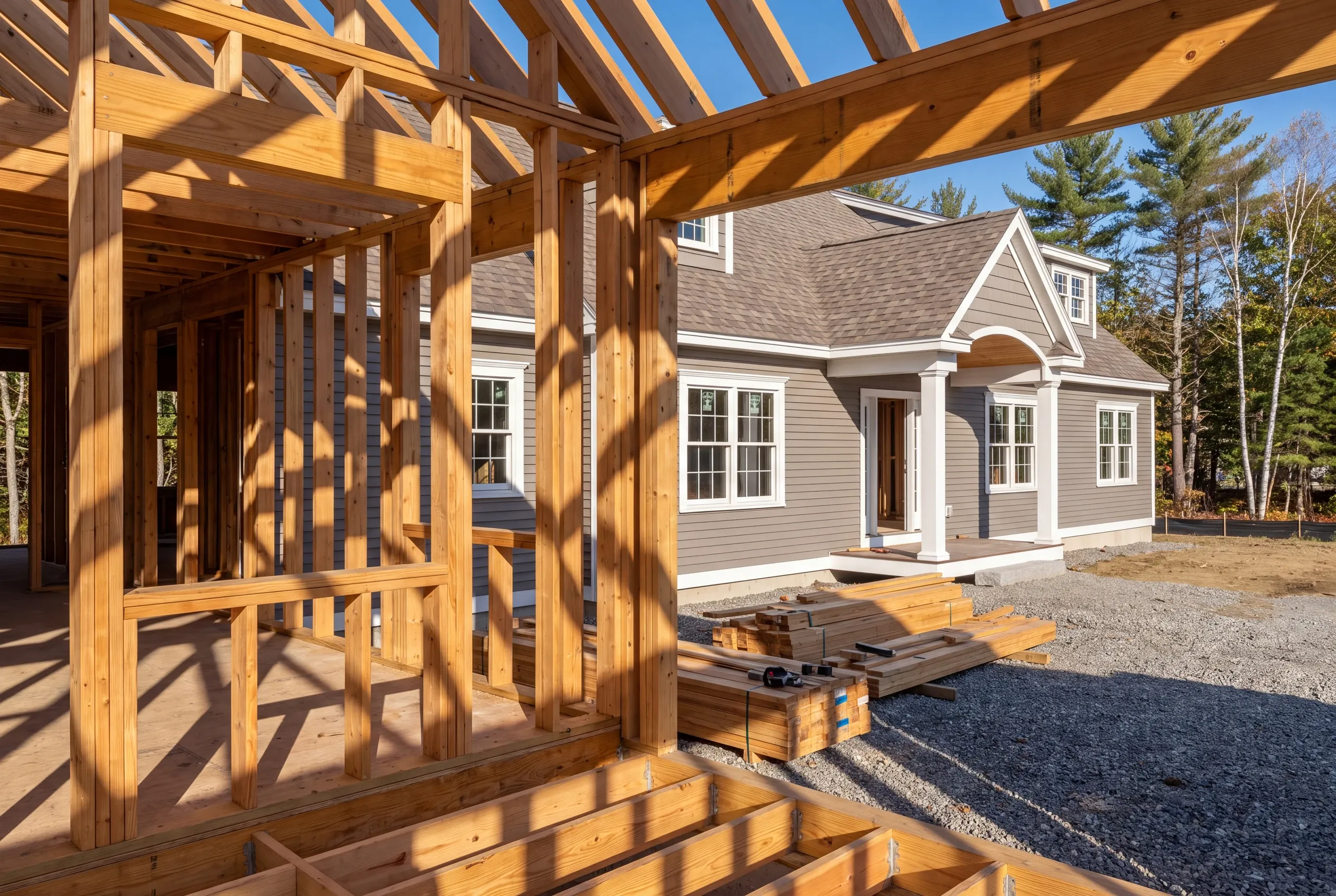 New home builder Gardiner Maine: open stud walls, rafters and floor joists in the foreground with a finished gray cape behind