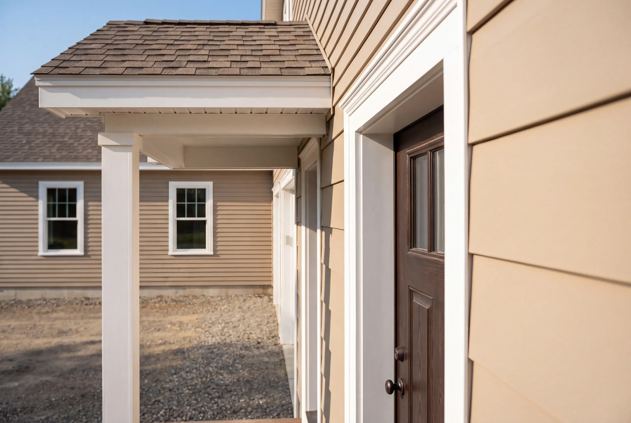 New home builder Pittsfield Maine: close view of a dark wood entry door, white trim and a square porch post on a tan house