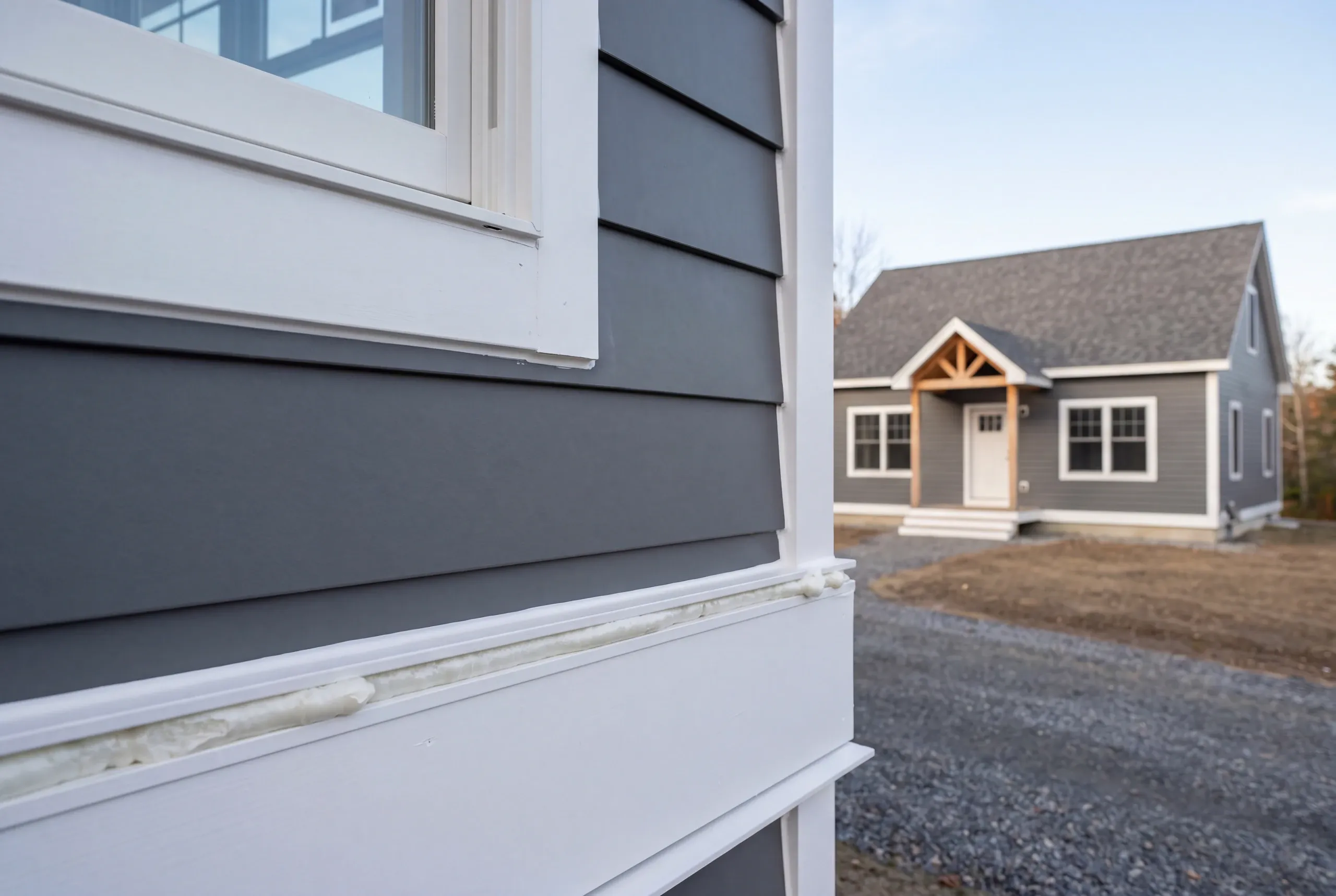 New home builder Thomaston Maine: close view of gray lap siding and white trim with foam in a trim joint, a cape behind