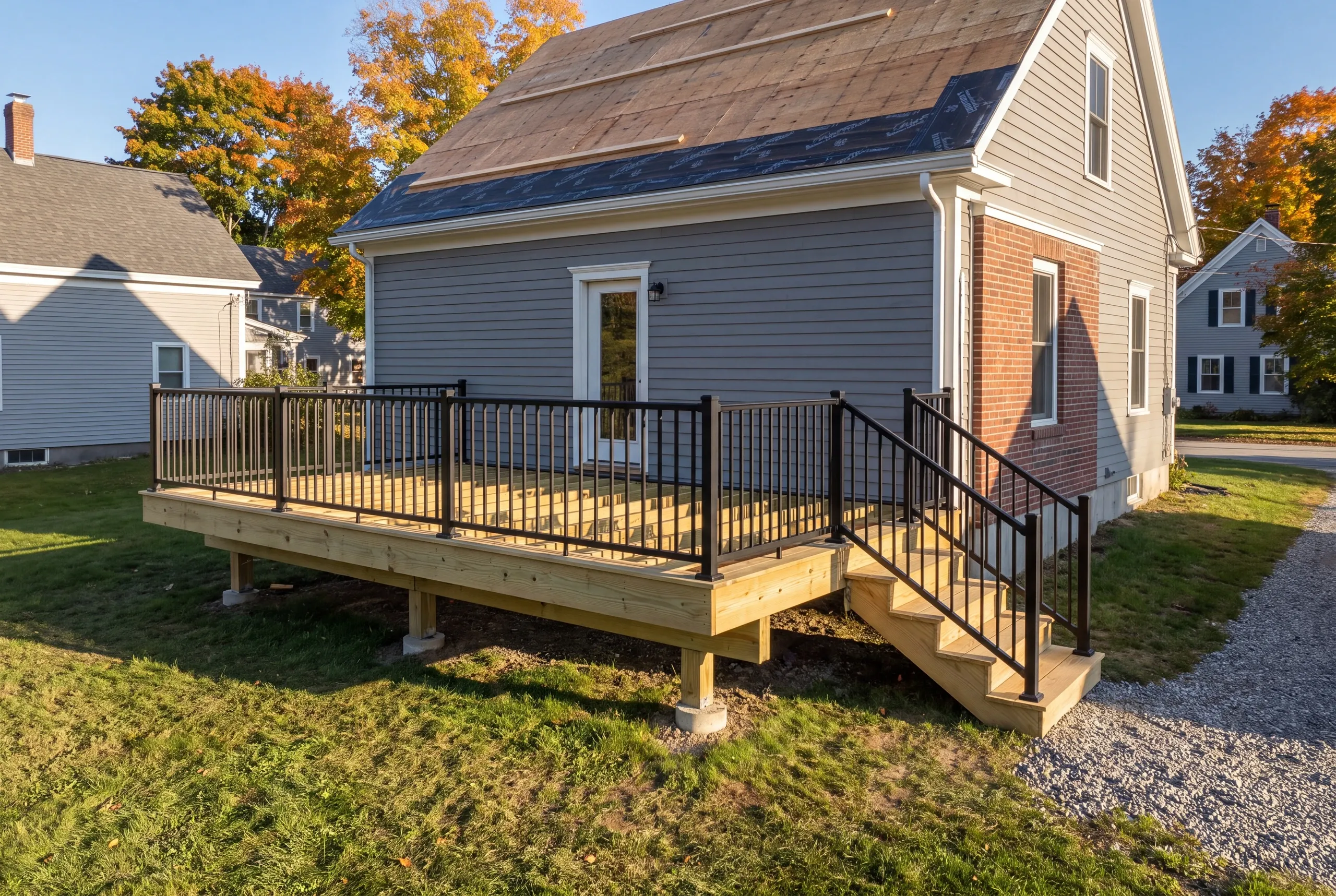 Deck contractor Damariscotta Maine: deck with black railing on a blue-gray cape with roof partly in underlayment
