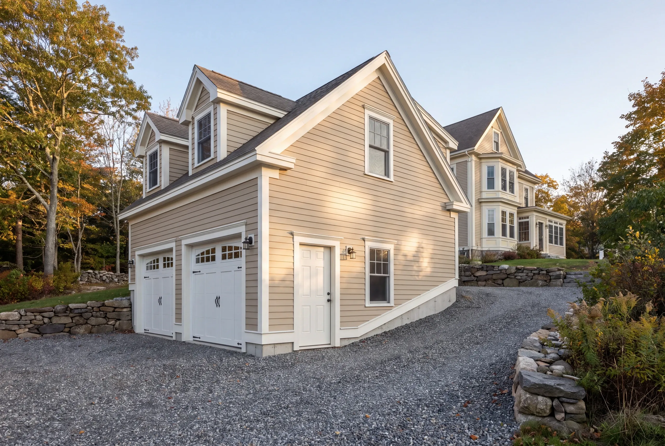 Garage builder in Belfast, ME: two-bay garage with dormers and a side door below a Victorian, stone walls and gravel drive