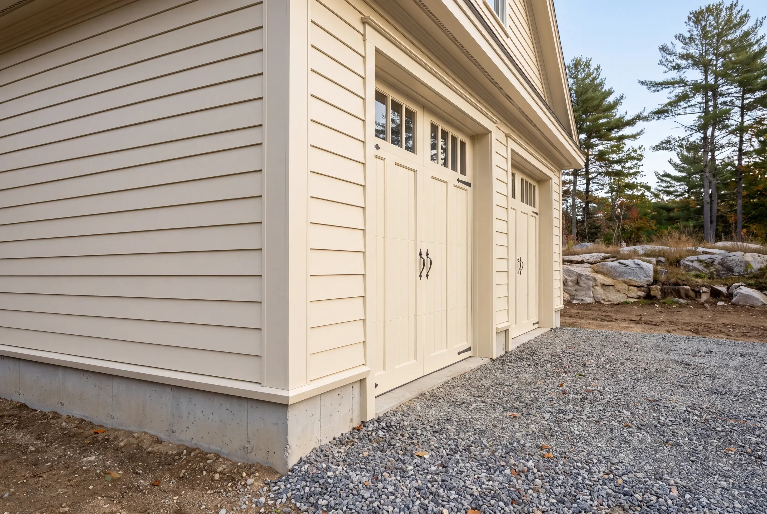 Custom garage builder Camden Maine: cream lap siding and carriage-style doors on a two-story garage beside a gravel drive