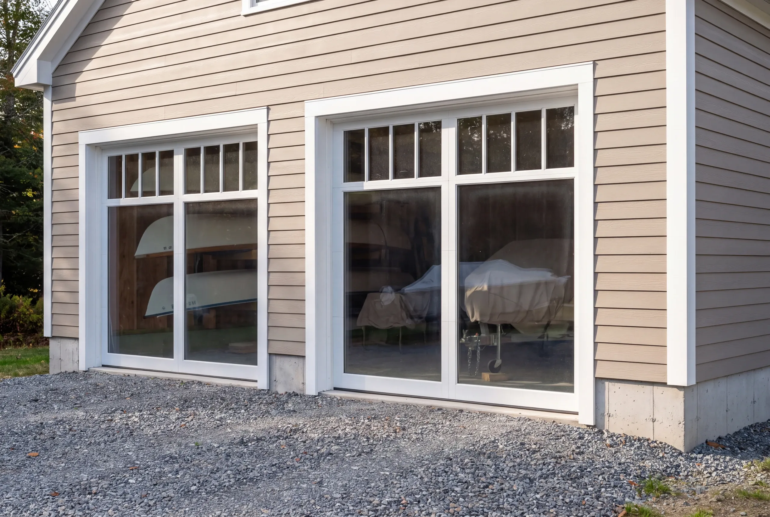 Custom garage builder Damariscotta Maine: glass-paneled garage doors showing stored boats and covered furniture inside