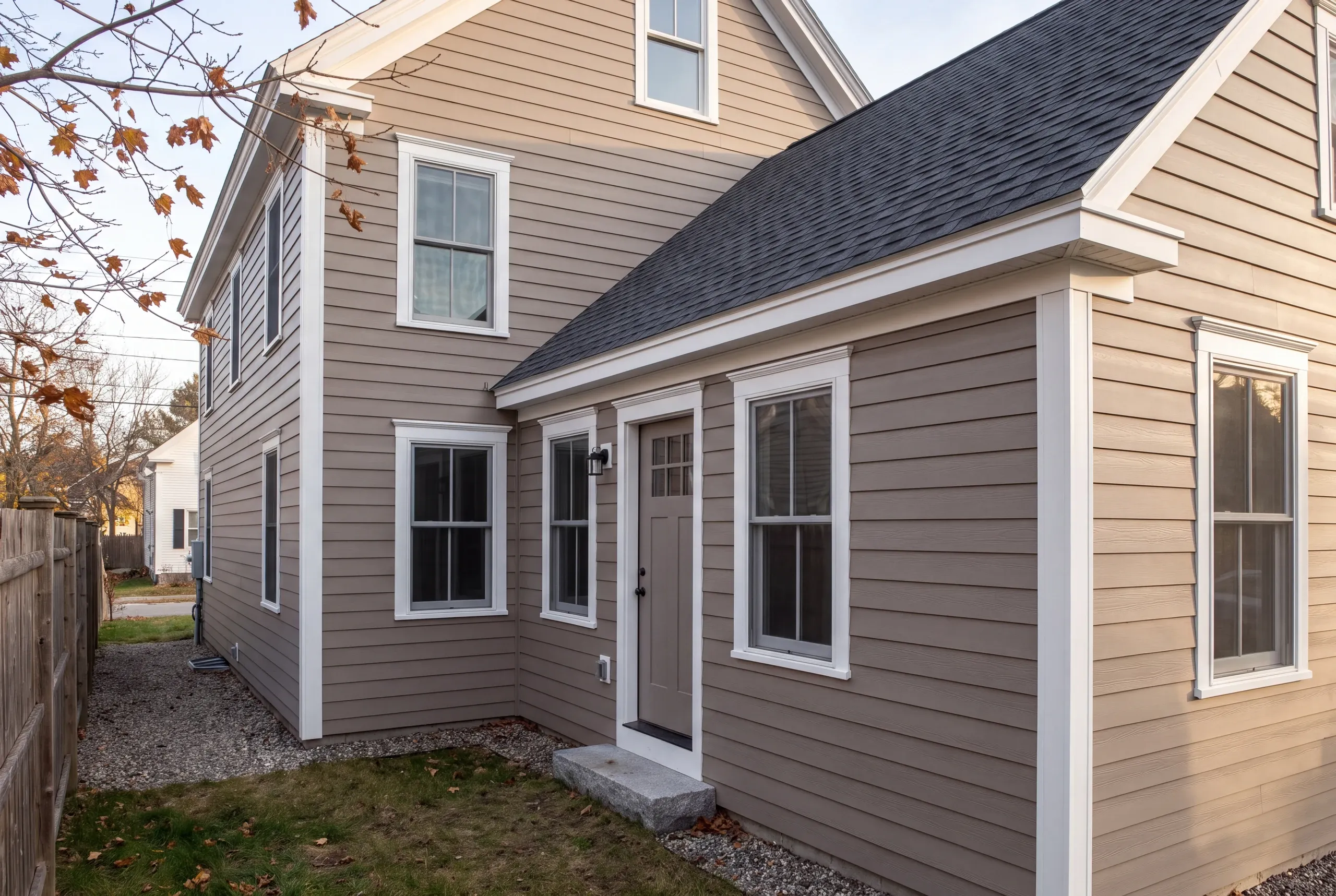 Residential general contractor Bath Maine: taupe lap two-story house with a gable wing, white trim and a fenced yard