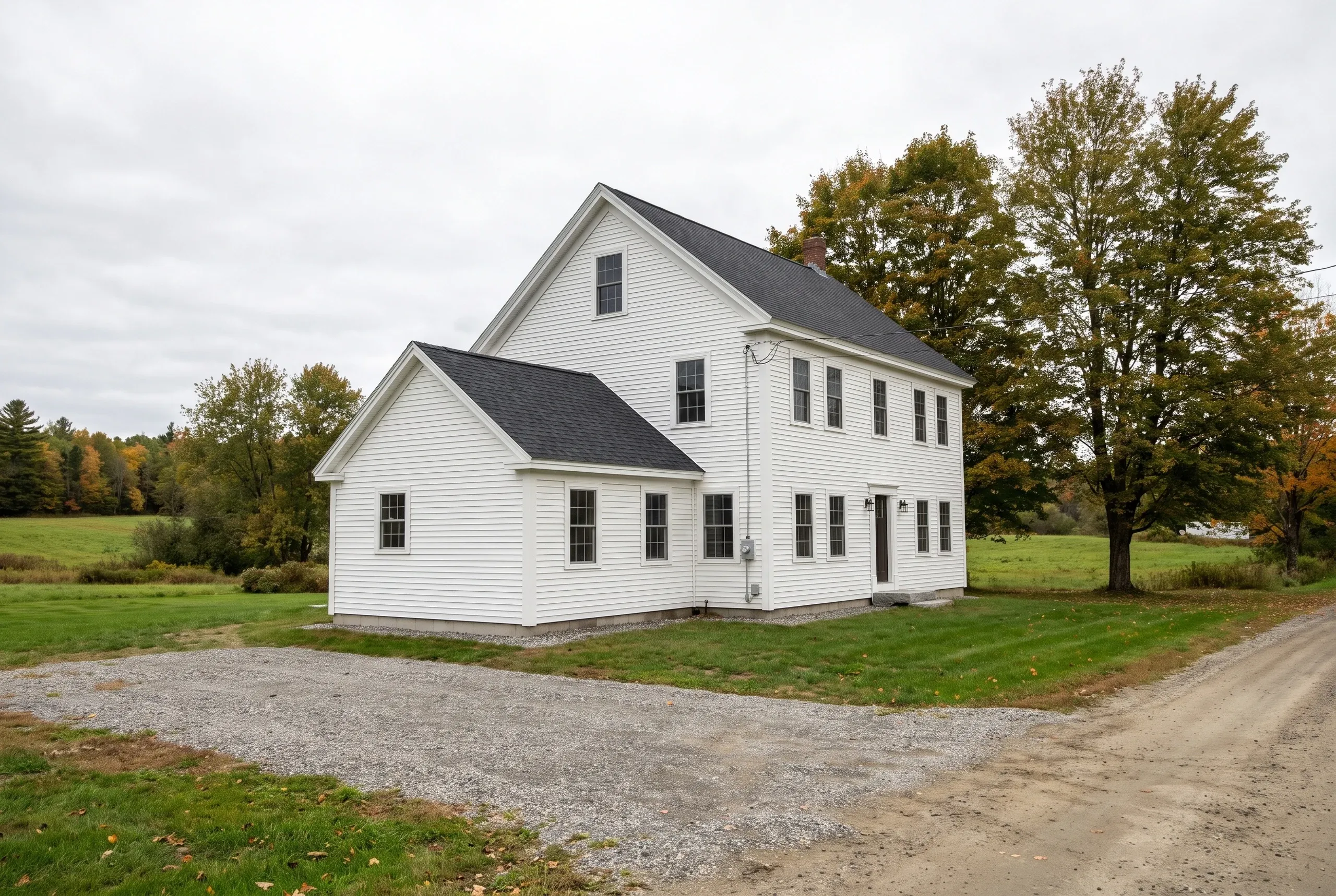 Residential general contractor Searsmont Maine: white clapboard colonial with a one-story side wing and a gravel drive in fall