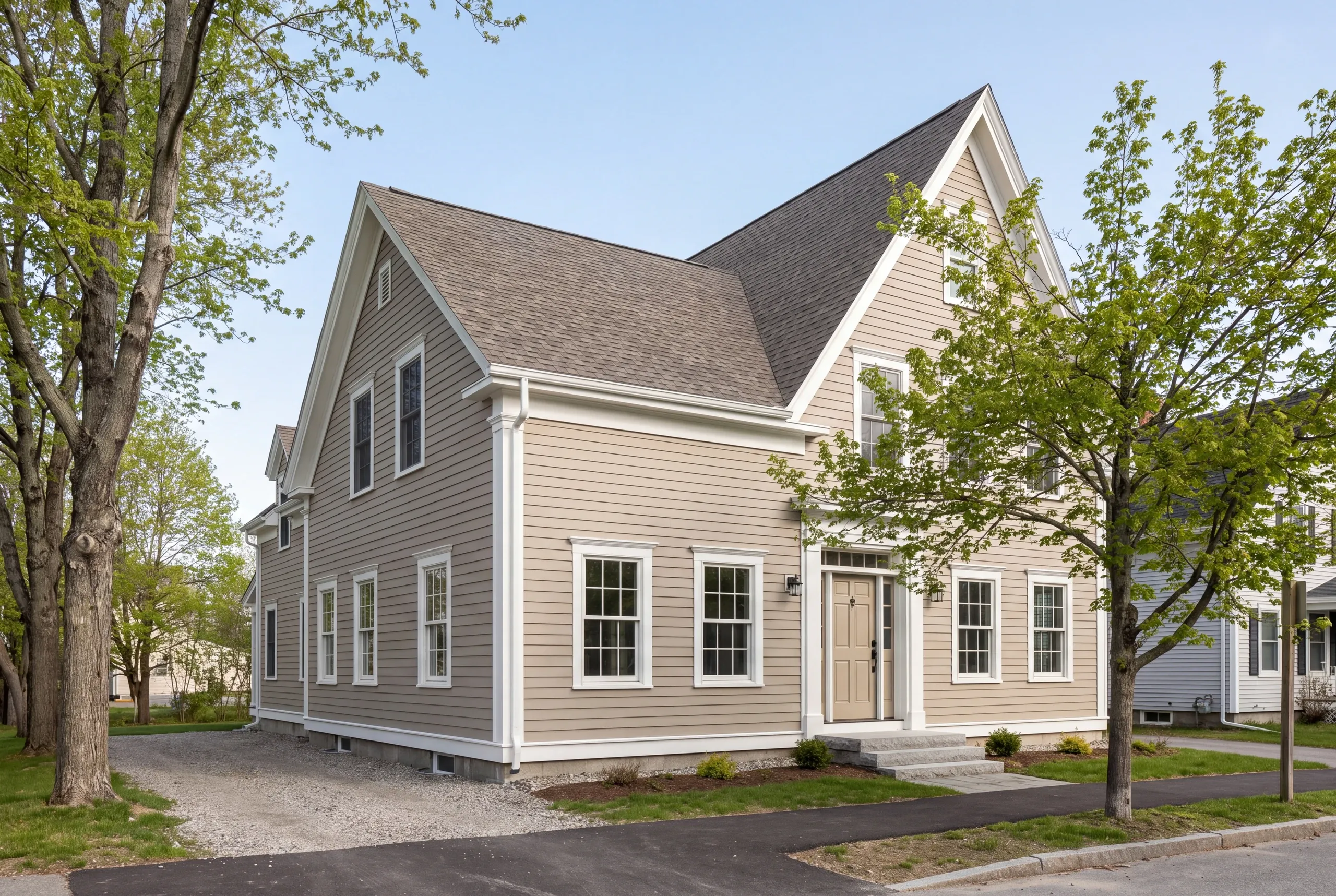 Construction company Waterville Maine: tan lap-sided two-story house with white corner boards and granite steps on a tree-lined street
