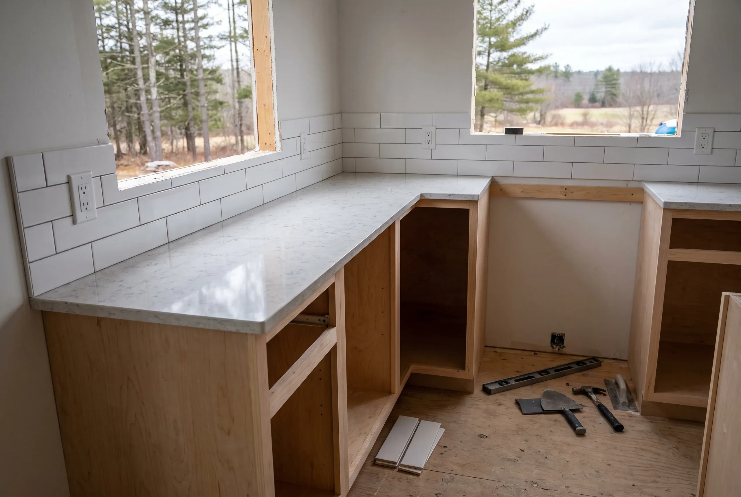 Kitchen remodeling contractor Augusta Maine: quartz-look L counter and subway tile on maple cabinet boxes, tile tools on the subfloor