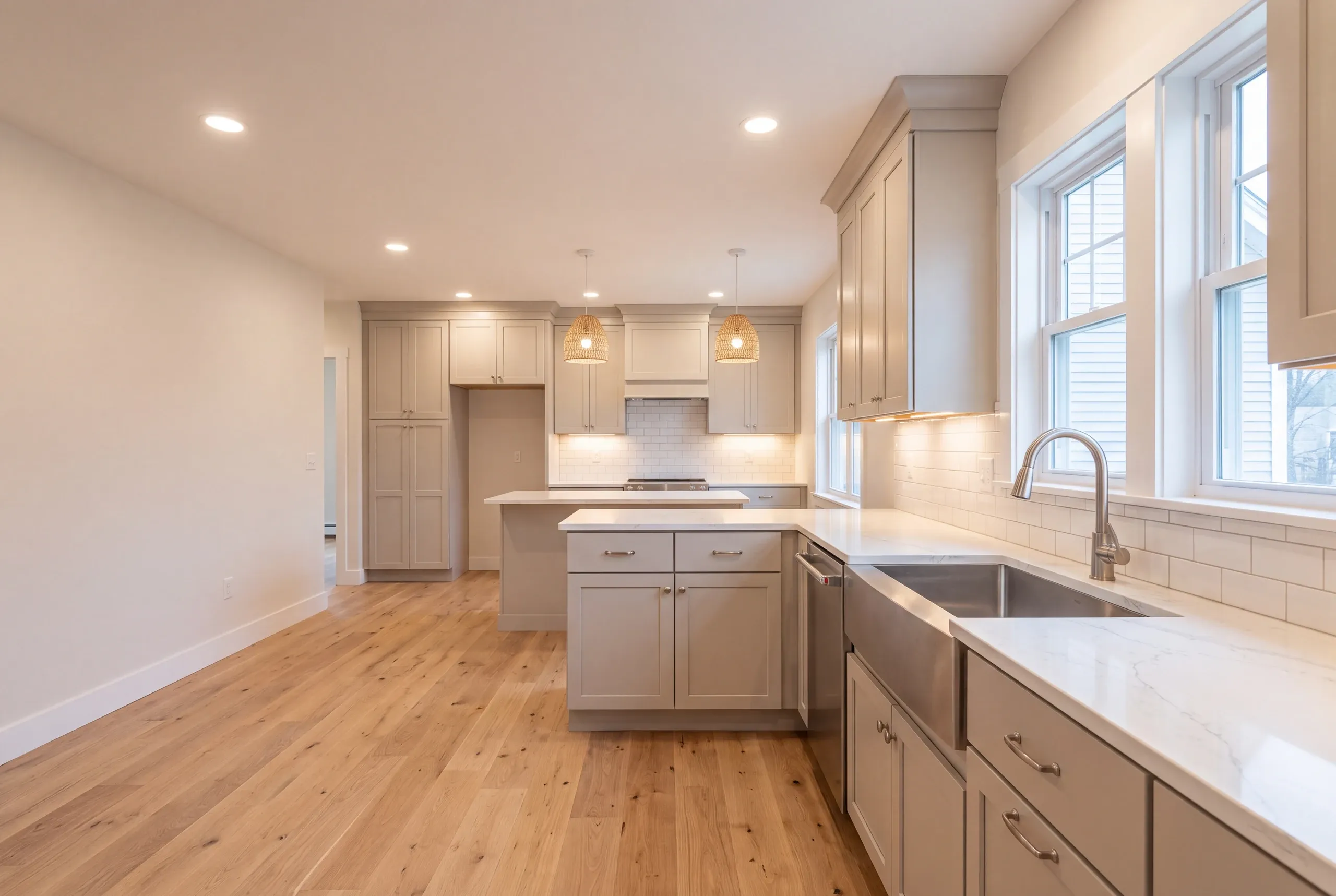 Kitchen remodeler Augusta Maine: open kitchen with greige shaker cabinets, a peninsula, woven pendant lights and an apron sink
