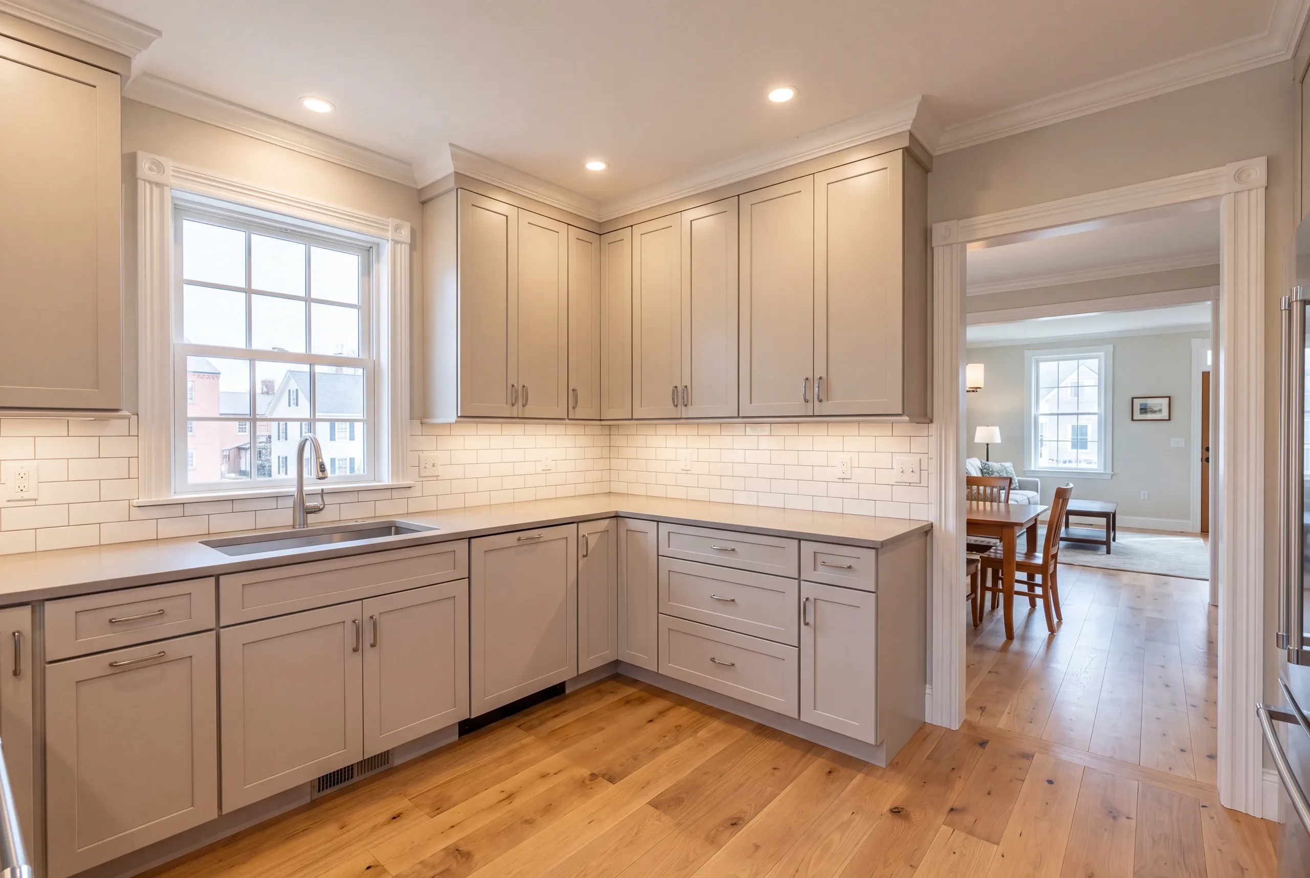 Kitchen remodeling in Bath, ME: corner run of greige shaker cabinets with gray counters and subway tile, opening to a dining room