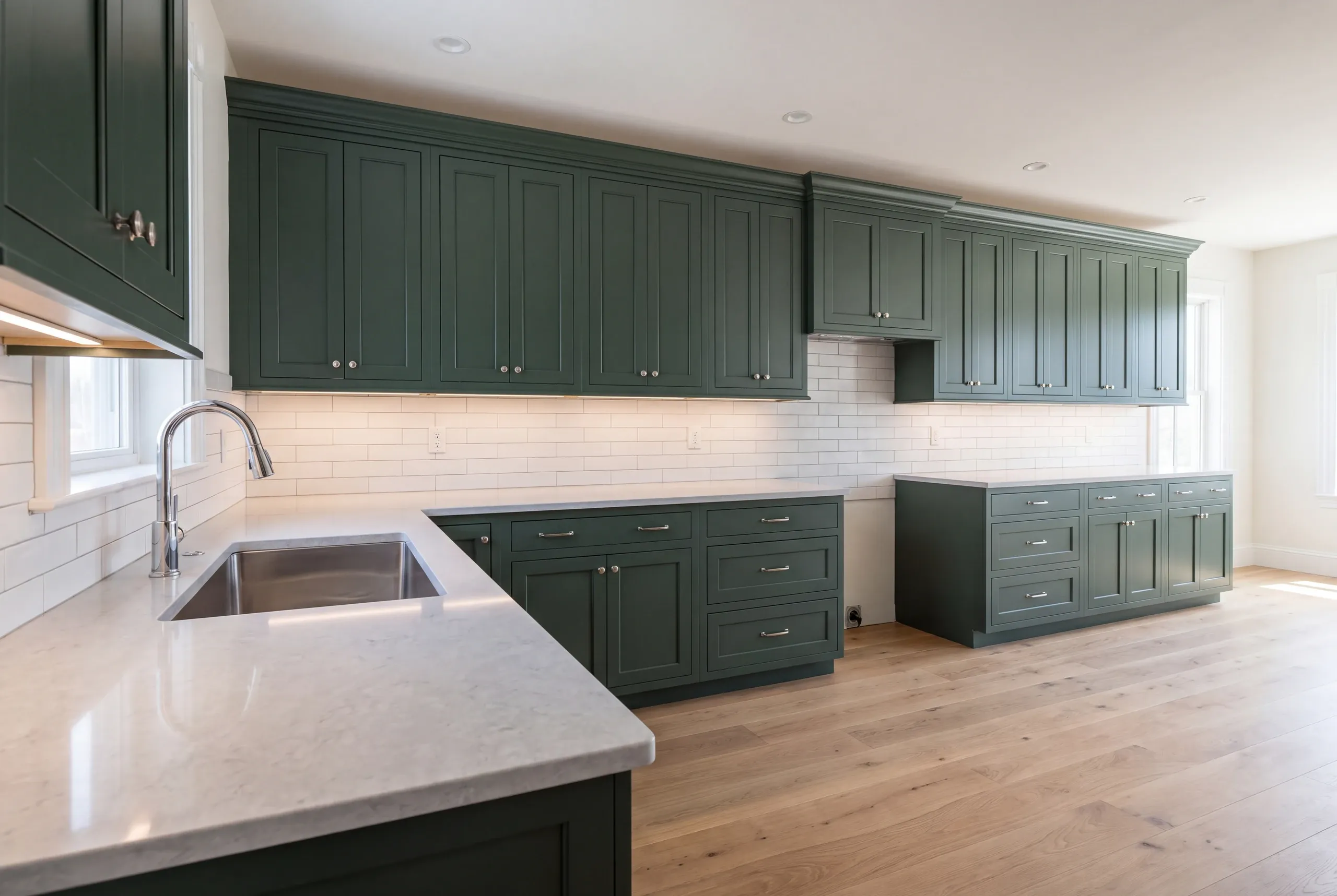 Kitchen renovation contractor Belfast Maine: long run of green inset cabinets with subway tile, quartz-look counters and wide oak floors