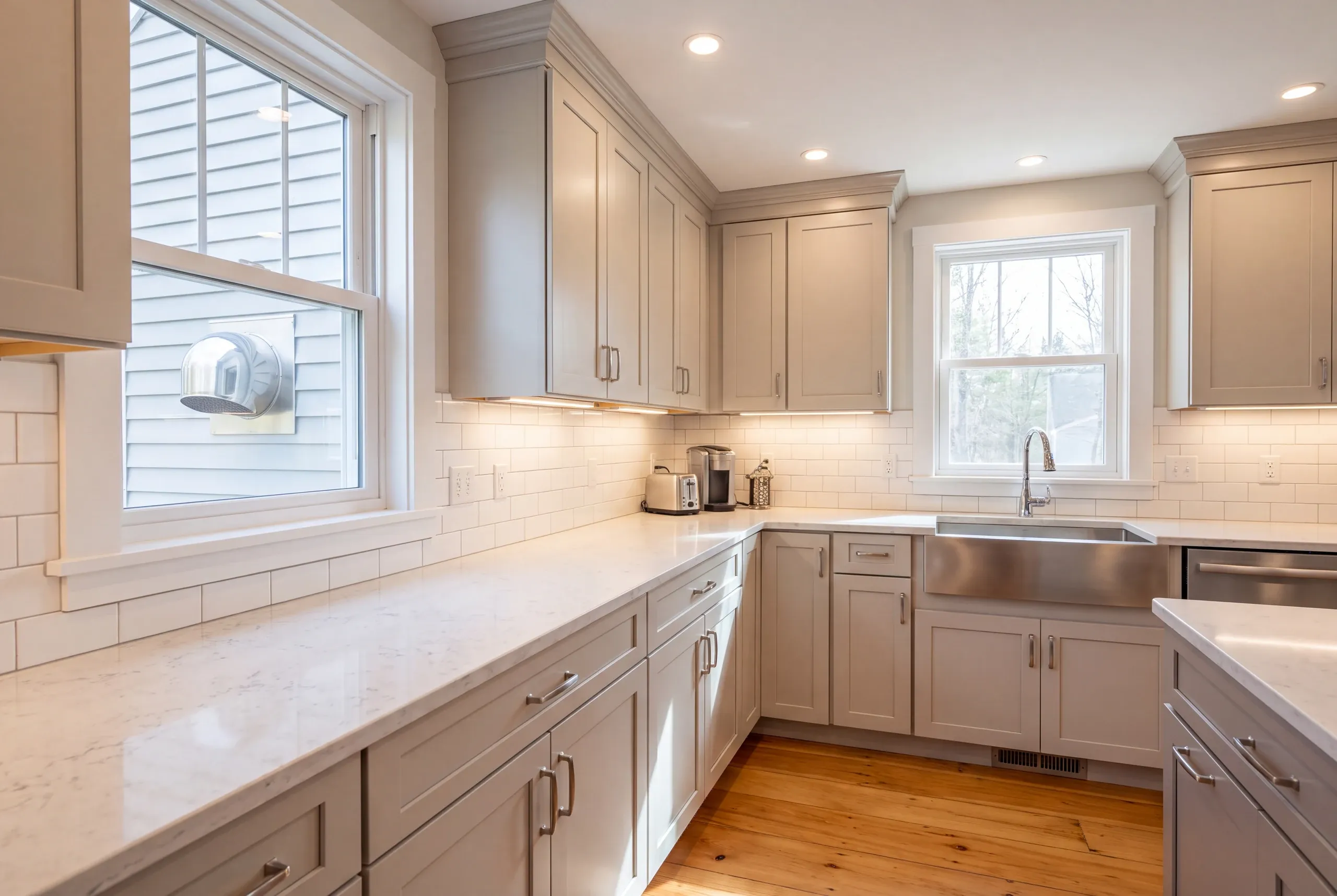 Kitchen remodeling contractor Bucksport Maine: greige shaker kitchen with a stainless apron sink, with a round wall vent cap visible outside
