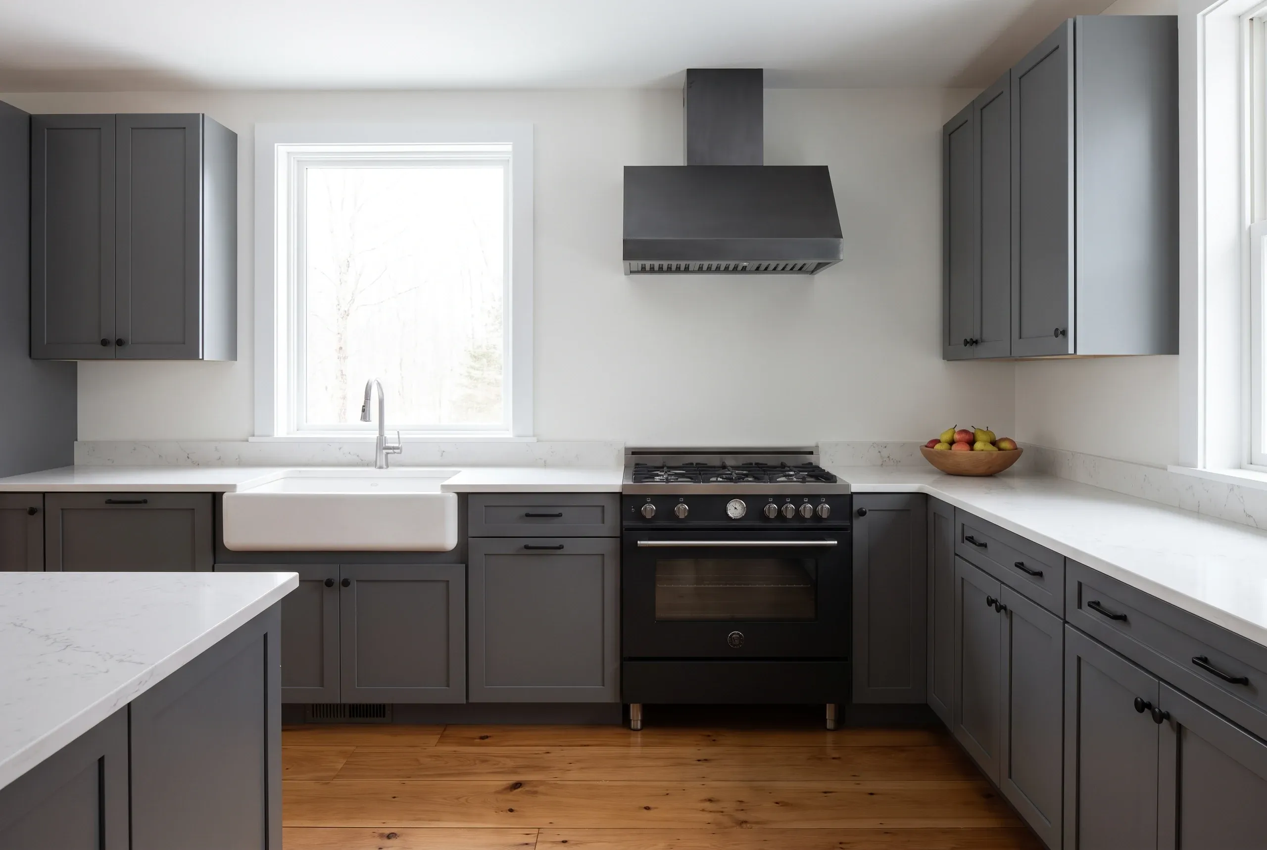 Kitchen renovation contractor Camden Maine: dark gray shaker kitchen with a white apron sink, black range and marbled quartz counters.