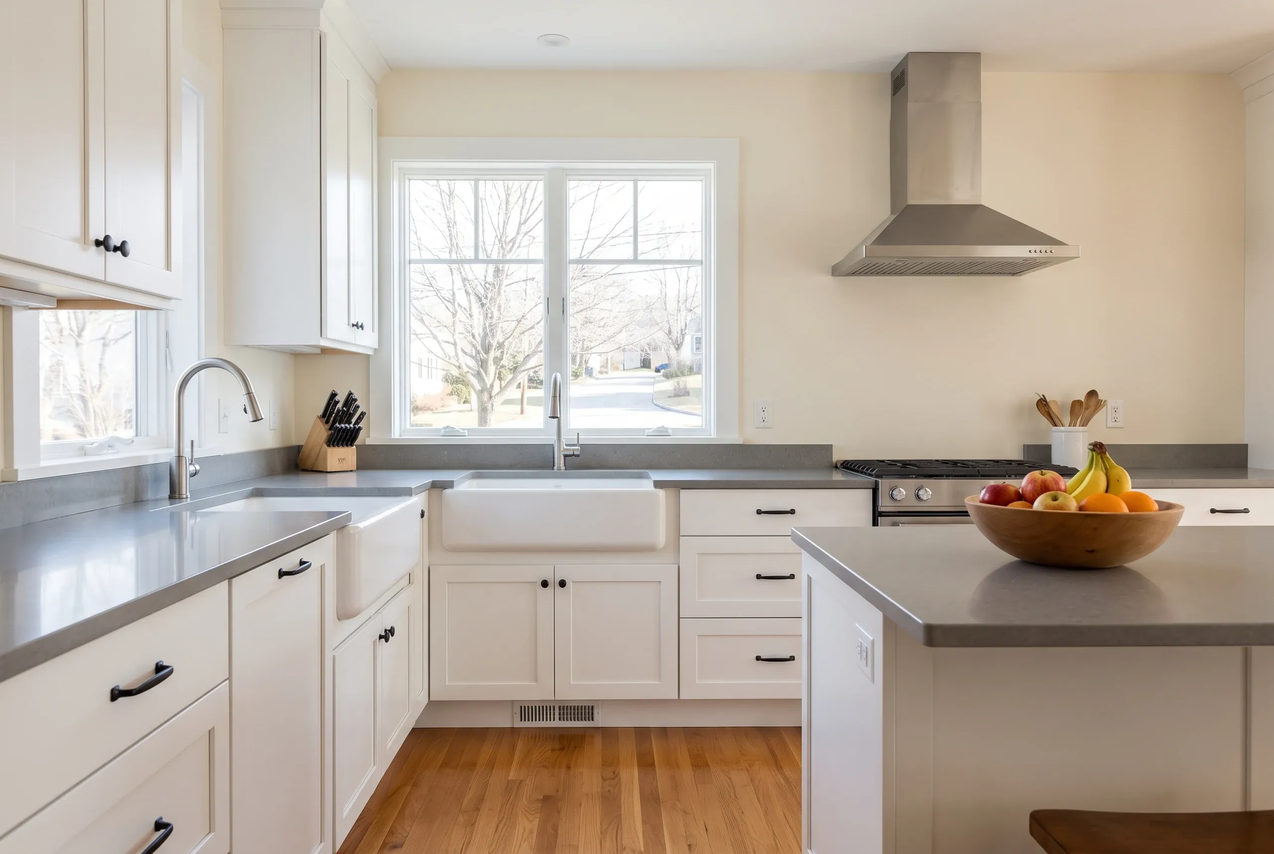 Kitchen remodeling contractor Camden Maine: white shaker kitchen with a fireclay apron sink, gray quartz counters and a double window.