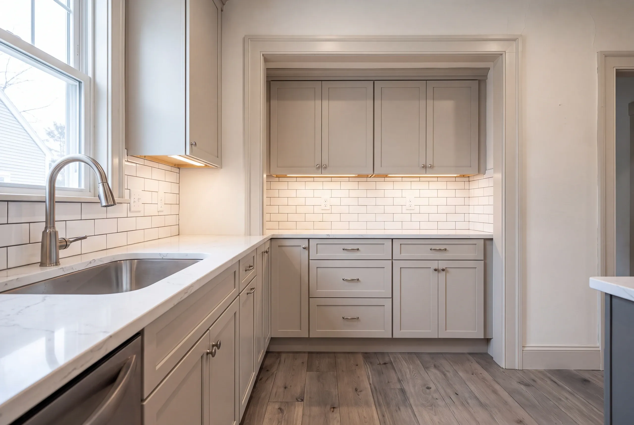 Kitchen renovation contractor Fairfield Maine: greige shaker cabinets set into a trimmed wall alcove with subway tile, undermount sink at left