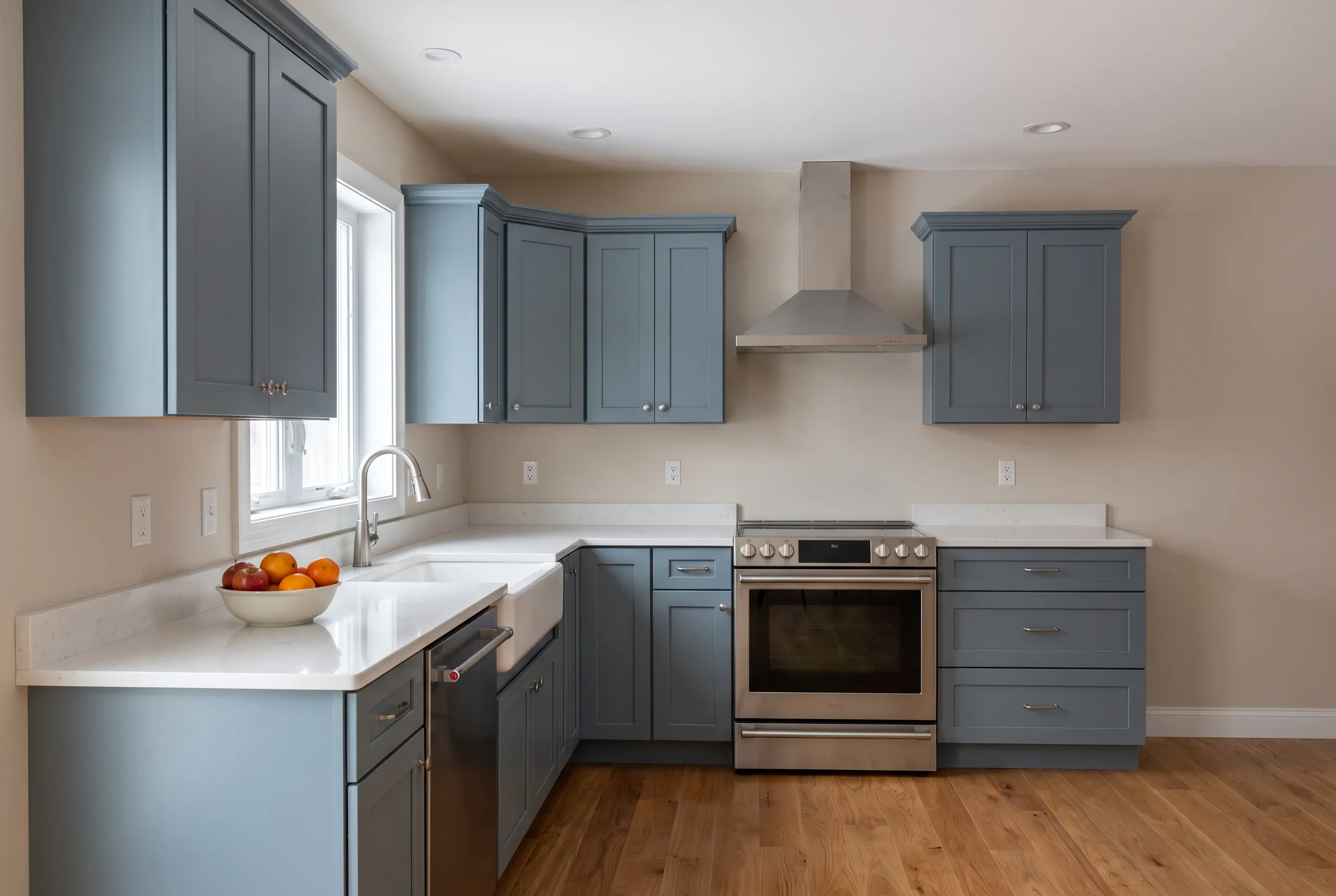 Kitchen remodeling contractor Fairfield Maine: slate blue shaker kitchen with white quartz counters, stainless range and a window over the apron sink.