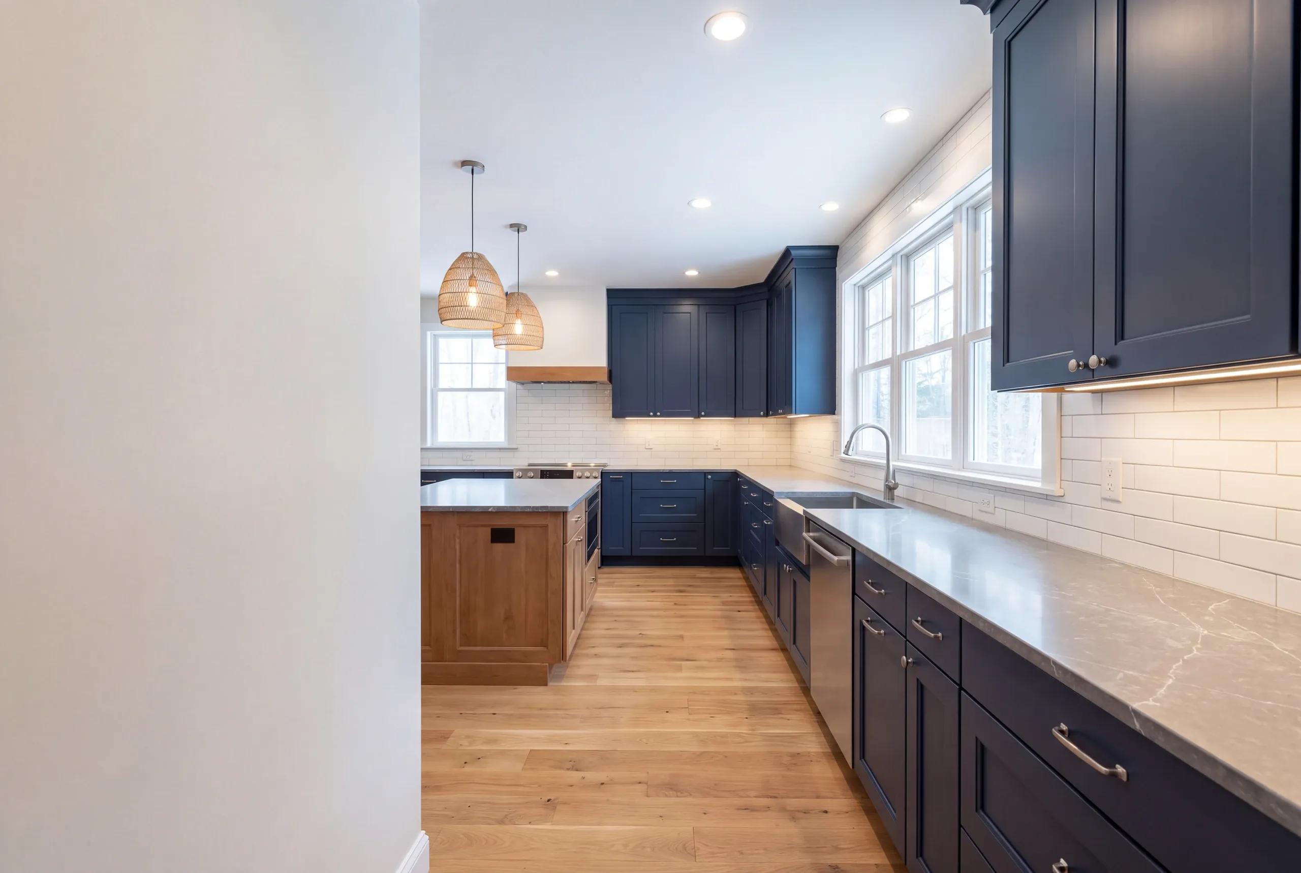 Kitchen remodeler Fairfield Maine: navy shaker cabinets with gray marble-look counters, a wood-toned island and woven pendants