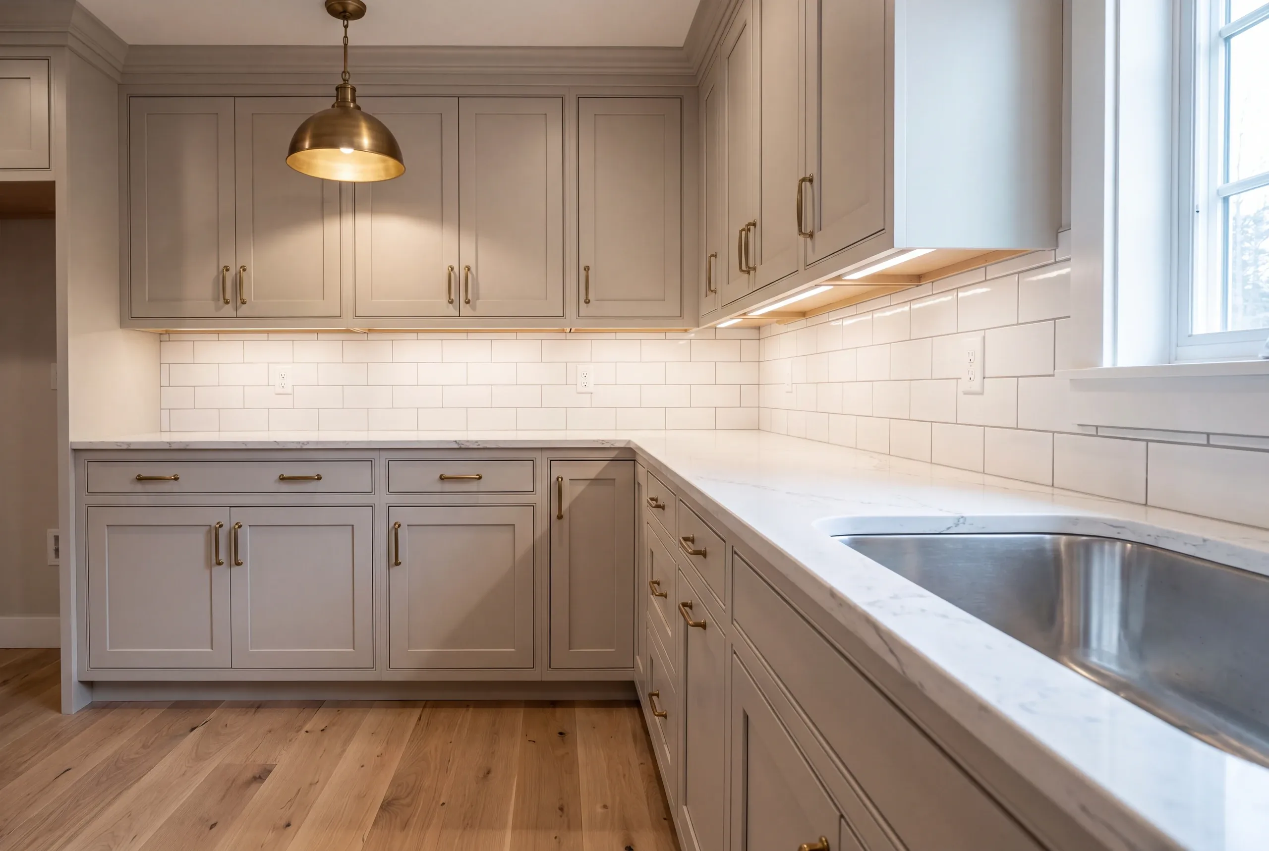 Kitchen renovation contractor Gardiner Maine: greige inset cabinets with brass bar pulls, a brass dome pendant and lit subway tile backsplash