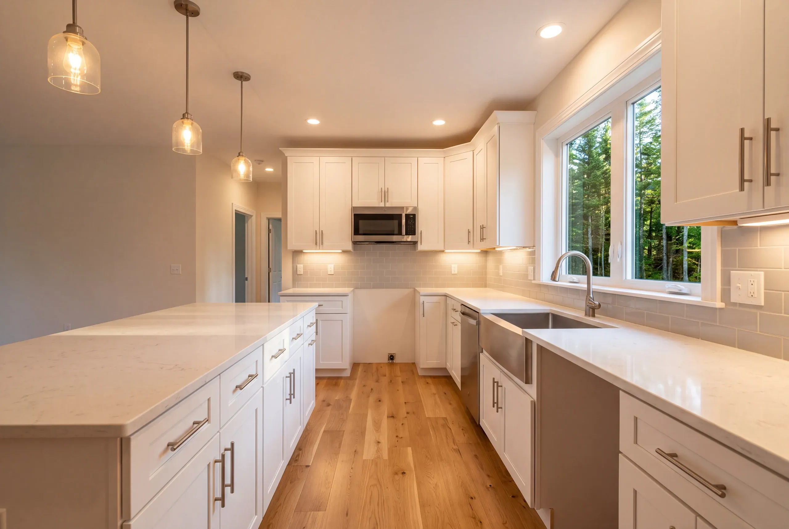 Kitchen remodeler Pittston Maine: white shaker kitchen with a stainless apron sink, over-range microwave and seeded glass pendants