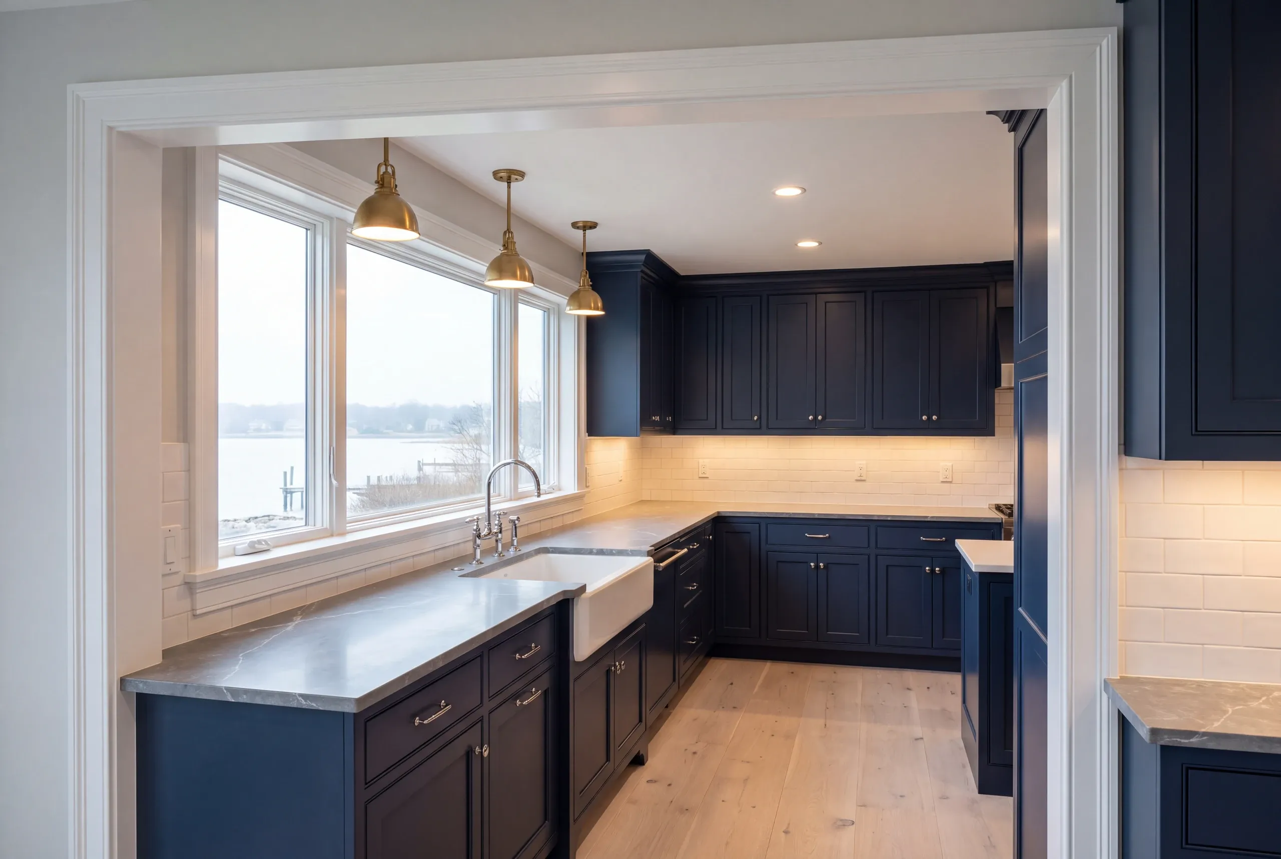 Kitchen remodeling contractor Rockport Maine: navy inset kitchen through a cased opening, brass pendants over a window by the water