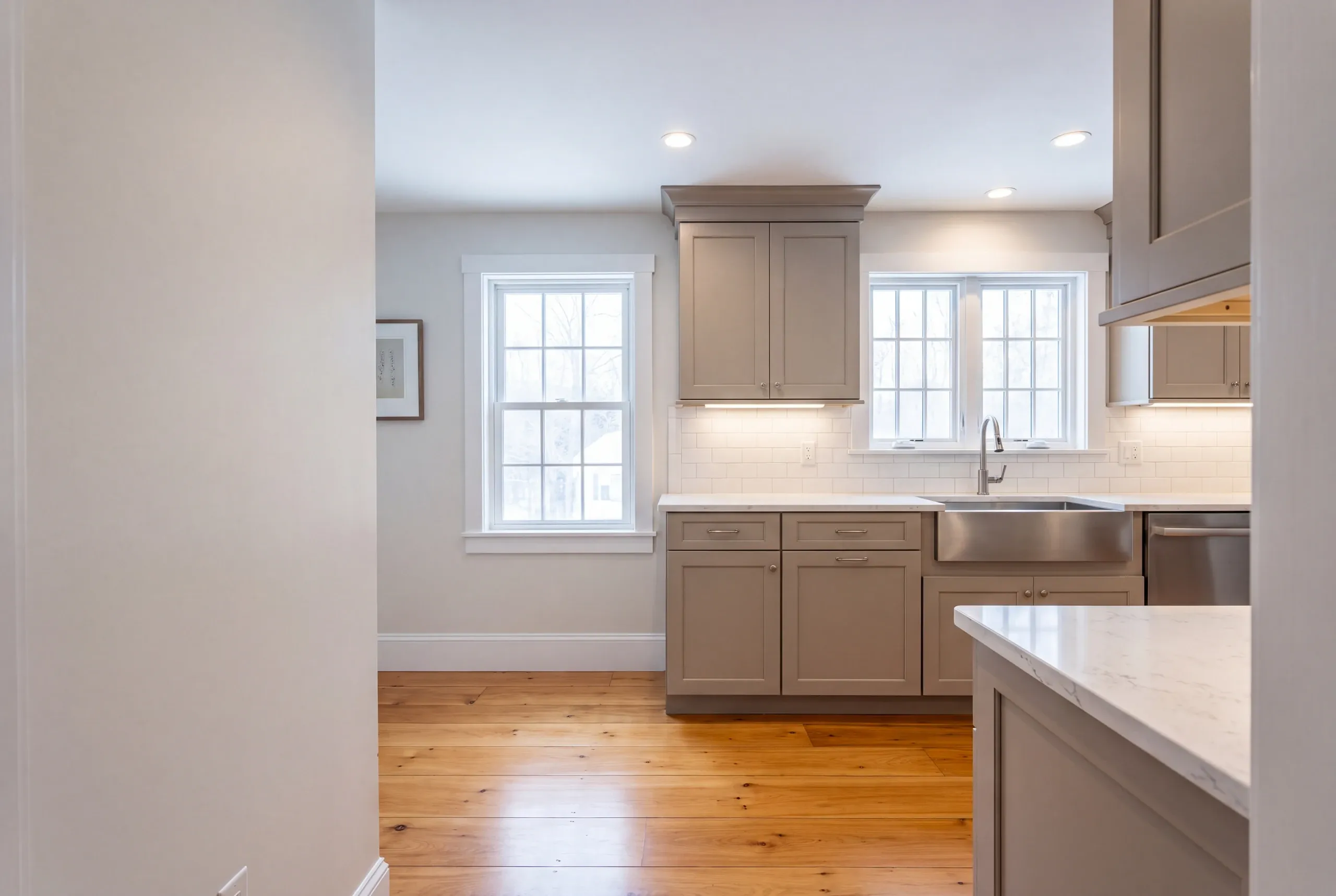 Kitchen remodeler Thomaston Maine: finished kitchen with greige shaker cabinets, steel apron sink and wide pine floors