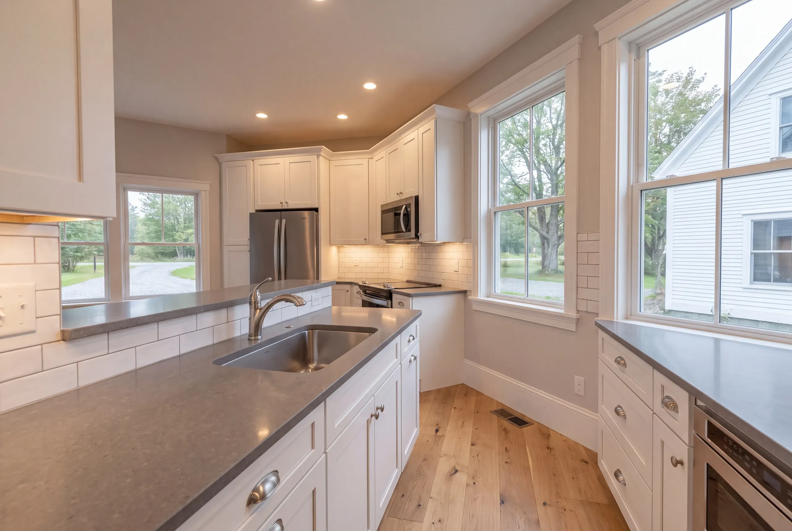 Kitchen remodeler Waldoboro Maine: white shaker kitchen with gray counters, stainless fridge and microwave, subway tile