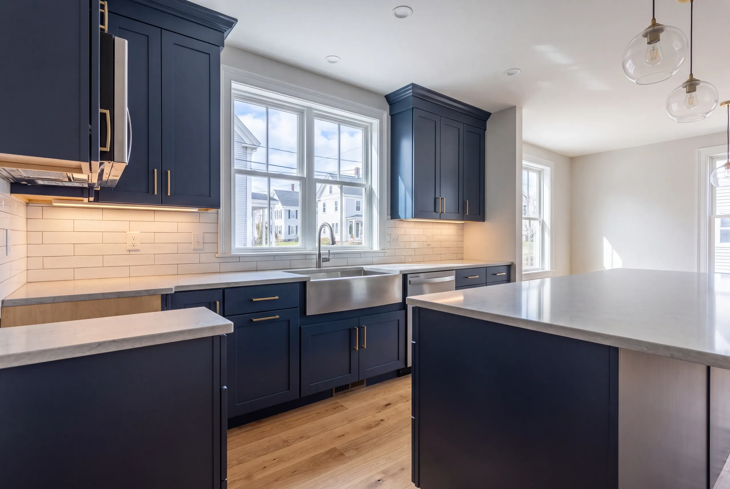 Kitchen remodeling contractor Waldoboro Maine: navy shaker cabinets with a steel apron sink, gray counters, island and glass pendants