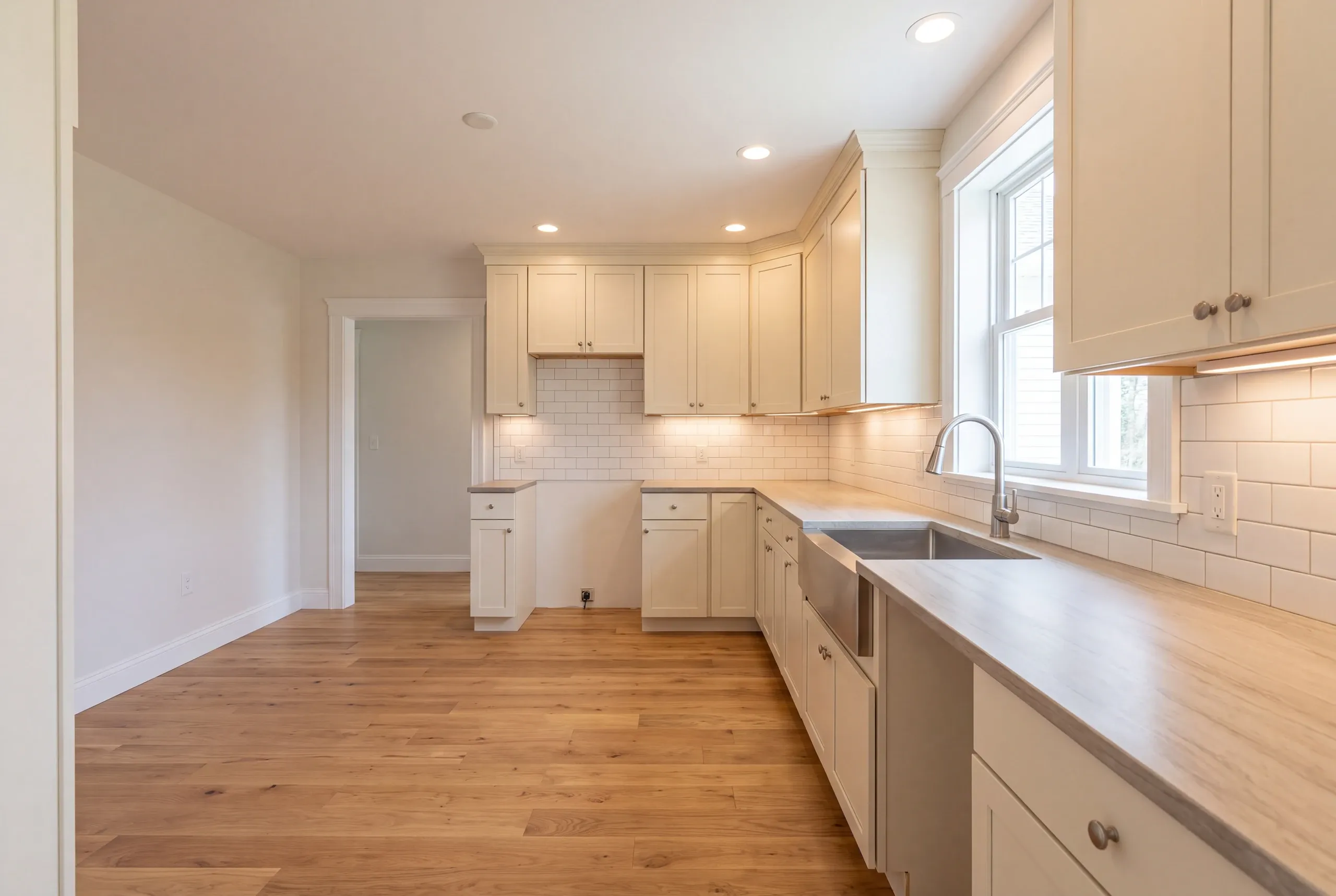 Kitchen renovation contractor Waldoboro Maine: empty finished kitchen with cream shaker cabinets, apron sink and wide oak floor