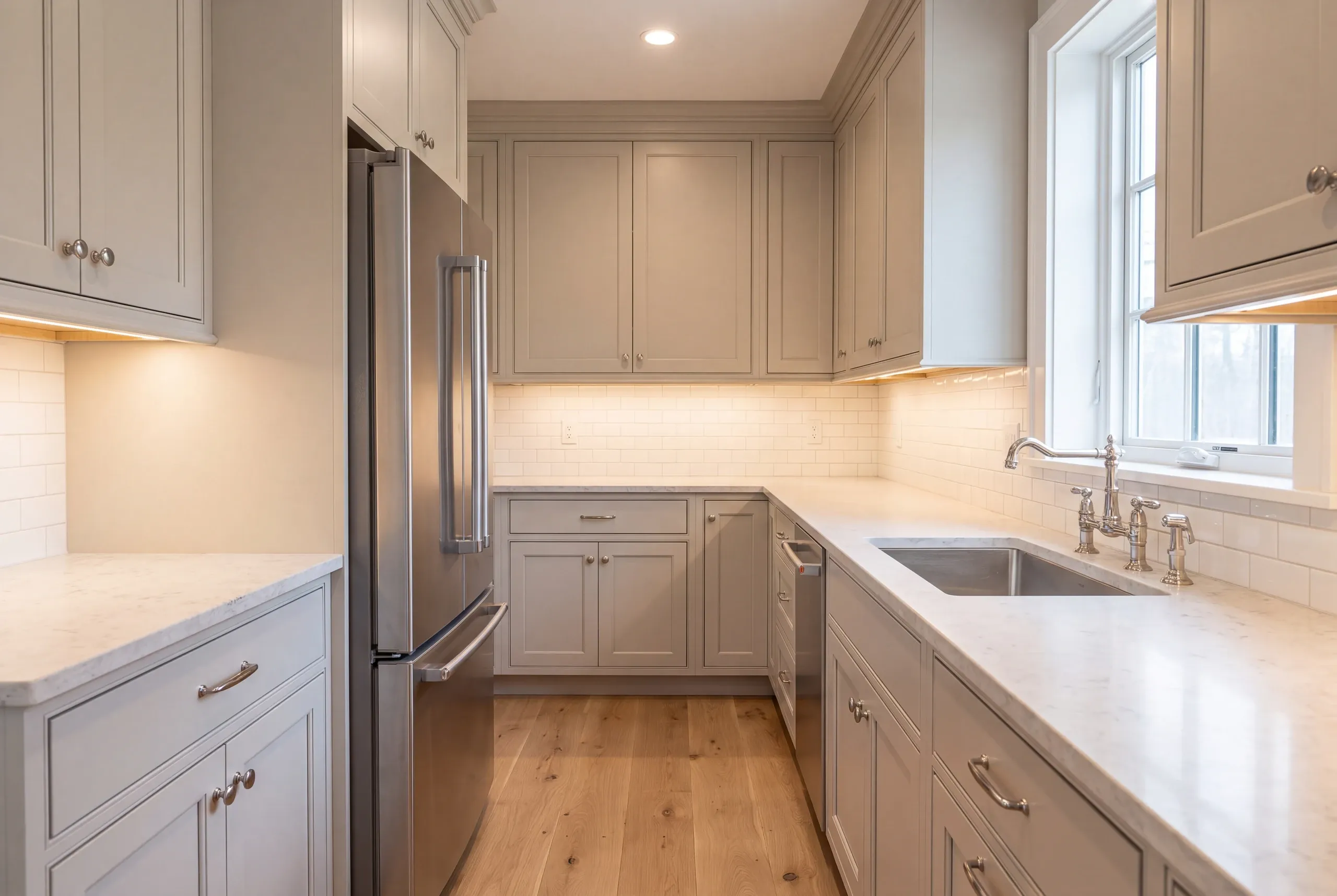 Kitchen renovation contractor Warren Maine: greige U-shaped kitchen with a stainless fridge, bridge faucet and quartz-look counters