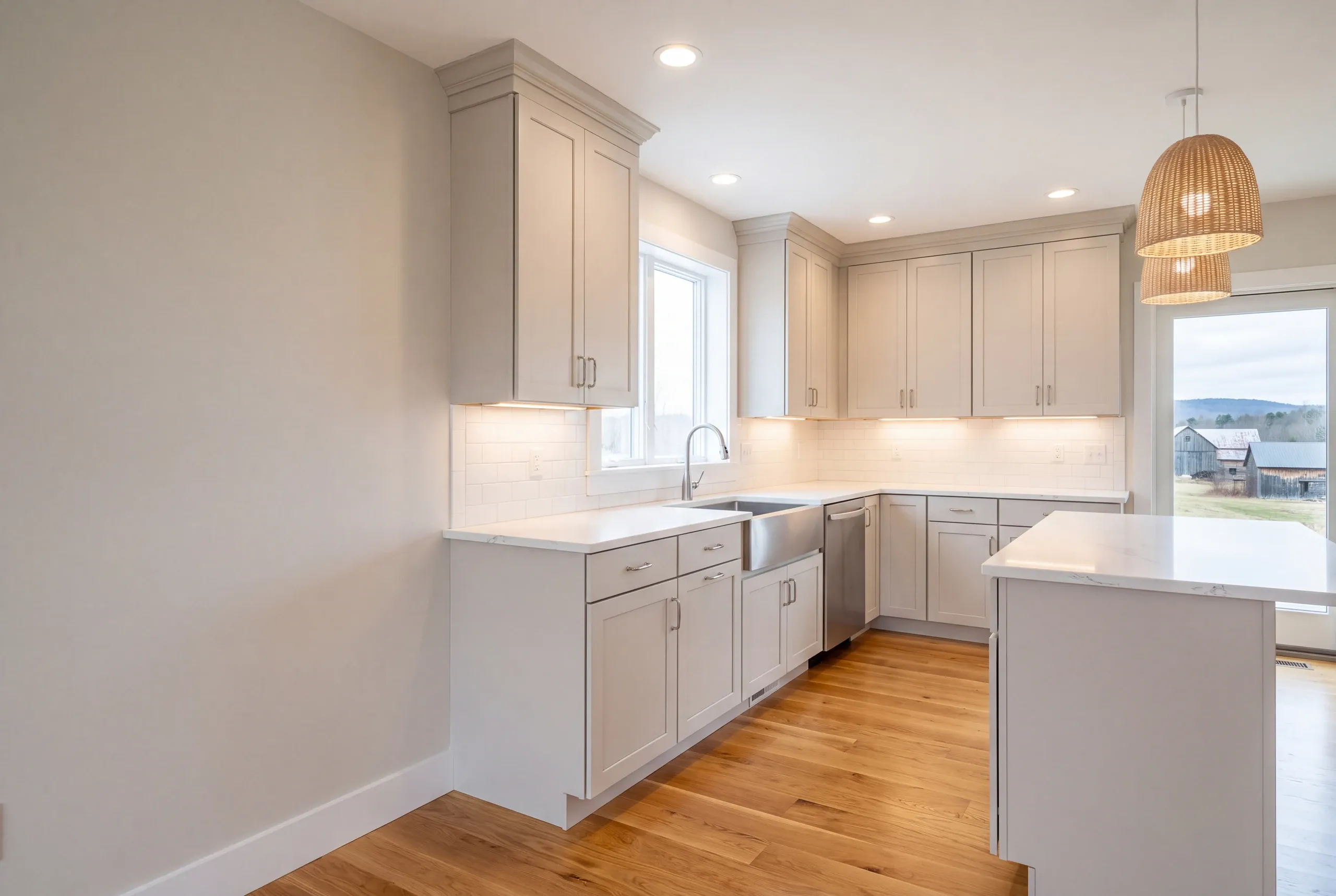 Kitchen remodeler Warren Maine: greige kitchen with woven rattan pendants, apron sink and a window toward farm buildings