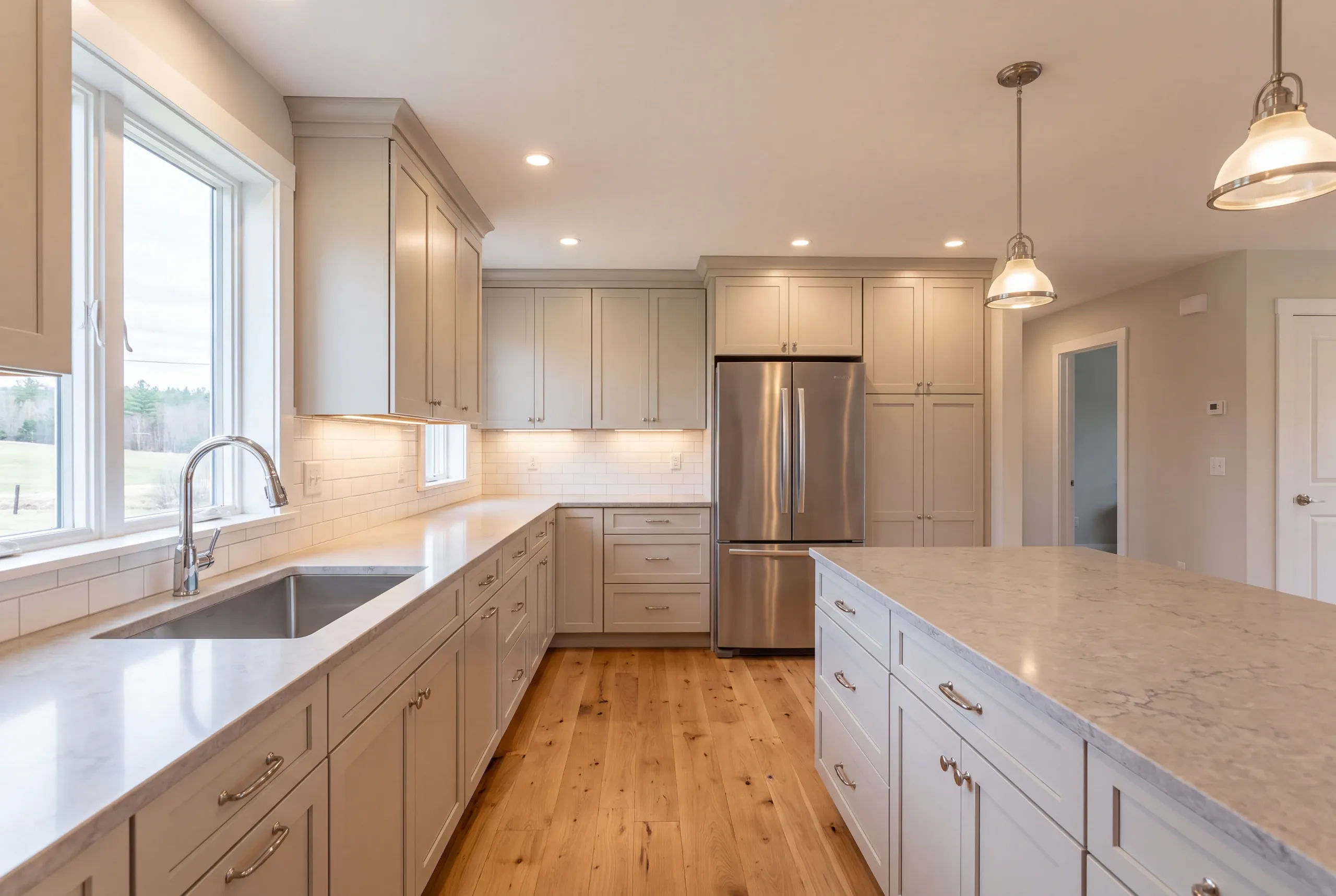 Kitchen renovation contractor Windsor Maine: light gray kitchen with a stainless fridge, marble-look island and two pendants