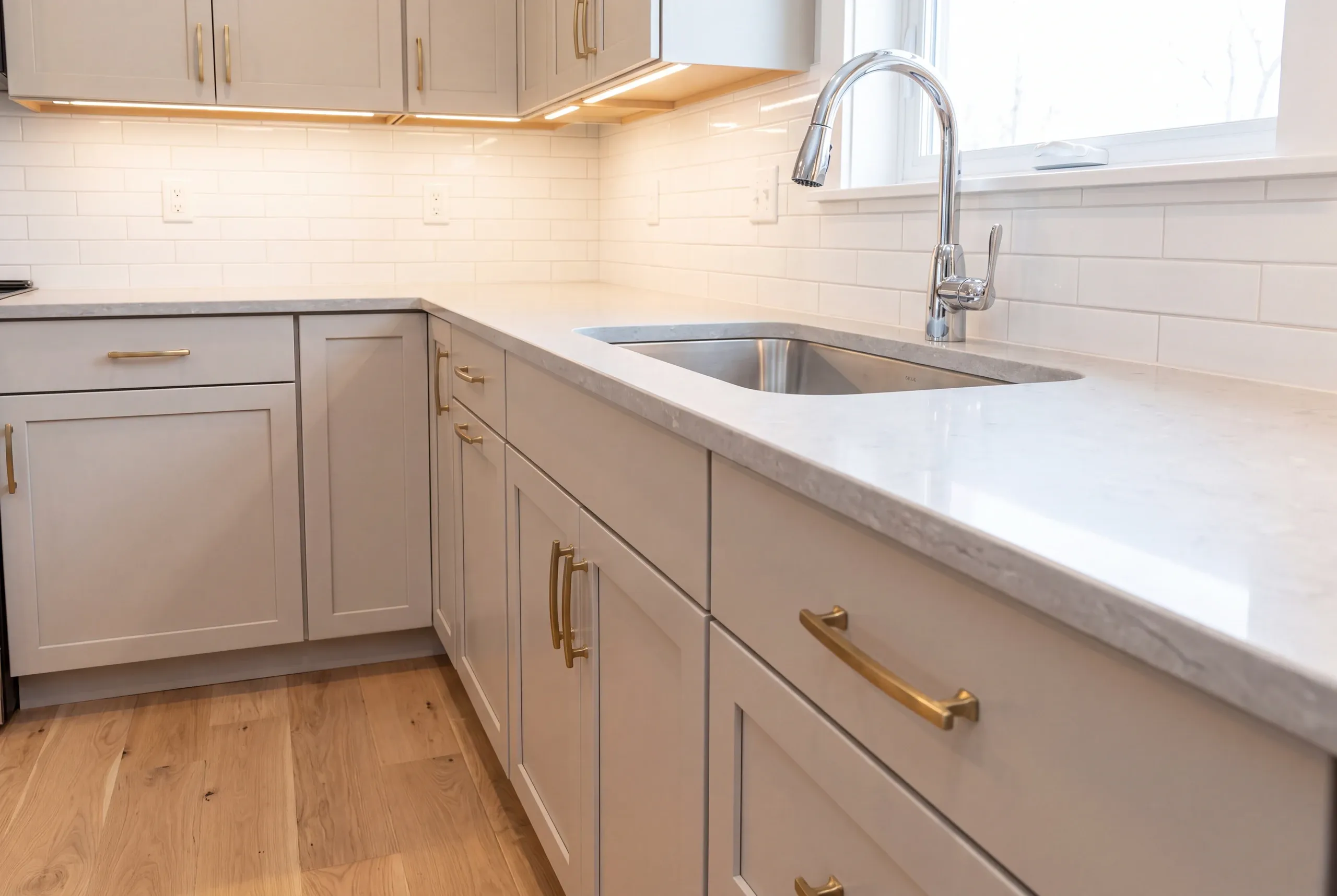 Kitchen renovation contractor Winslow Maine: light gray cabinets with brass bar pulls around an undermount sink and subway tile