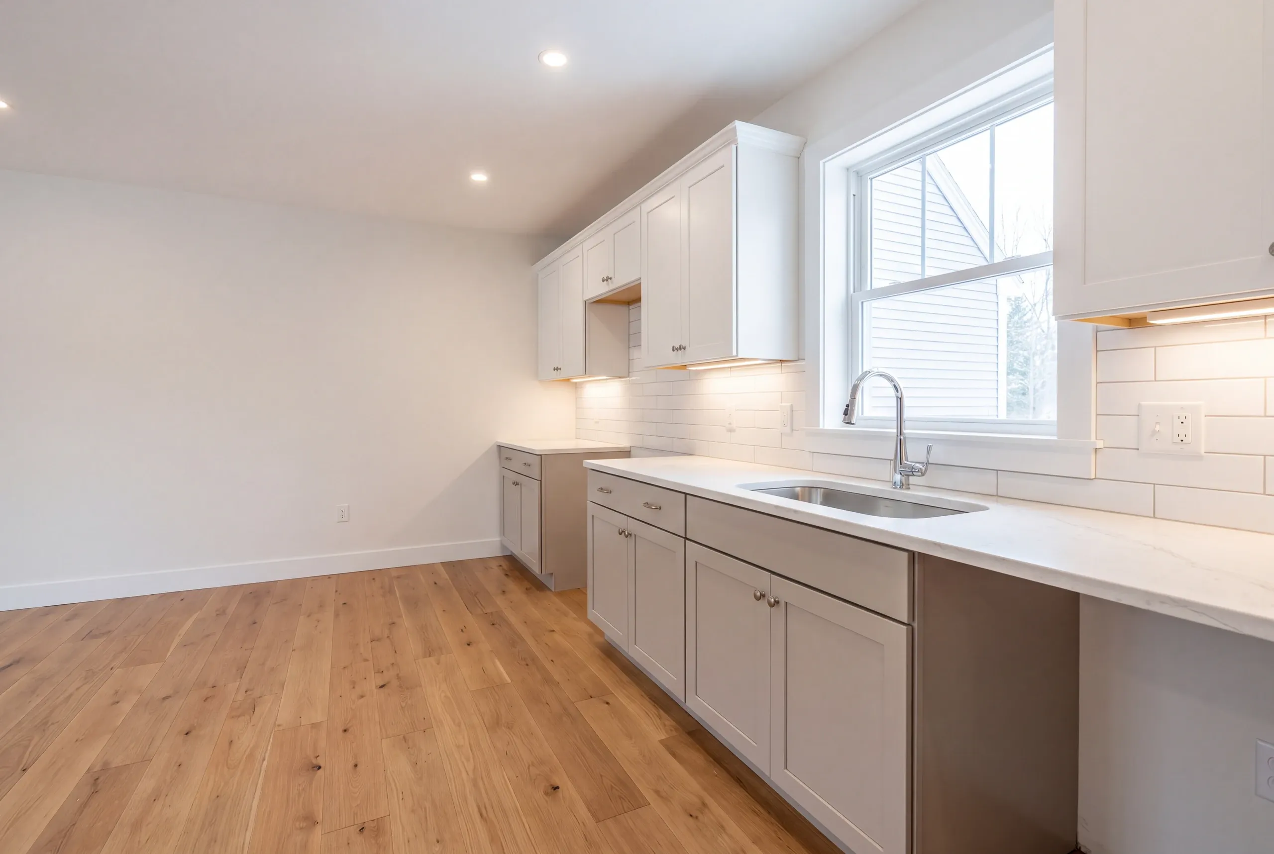 Kitchen remodeler Winslow Maine: empty white shaker kitchen with a long counter run under a double-hung window