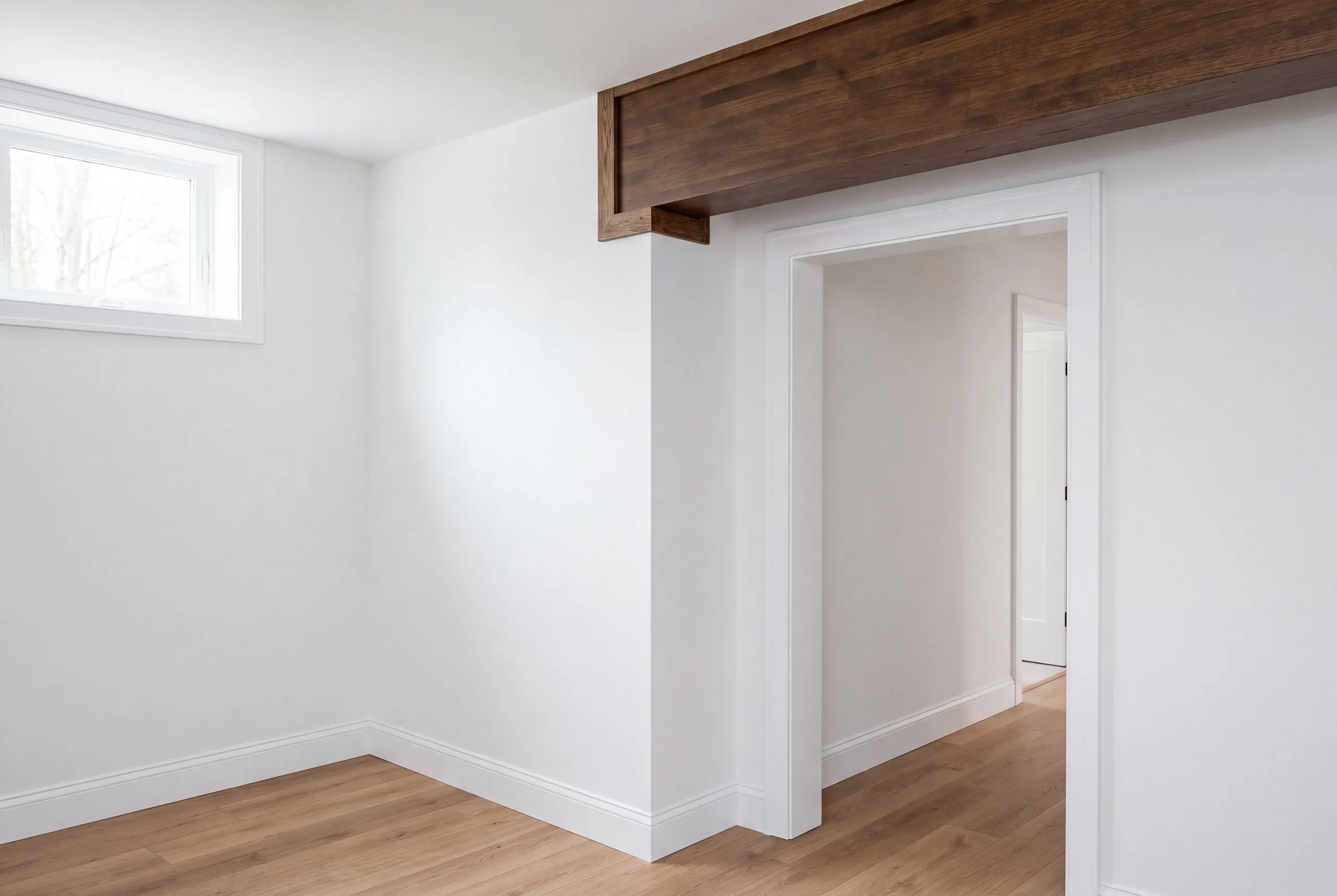 Home renovation contractor Augusta Maine: finished white room with a high basement window and a stained beam over a doorway