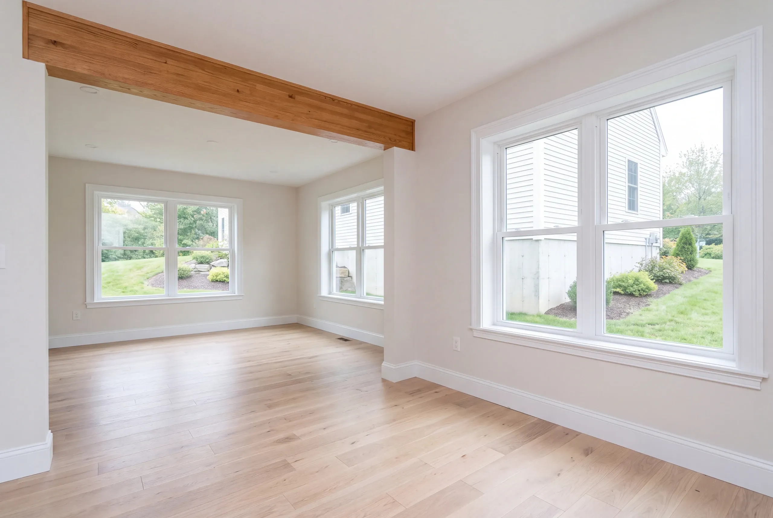 Remodeling company Augusta Maine: bright empty room with a natural wood beam and windows looking onto a sloped lawn