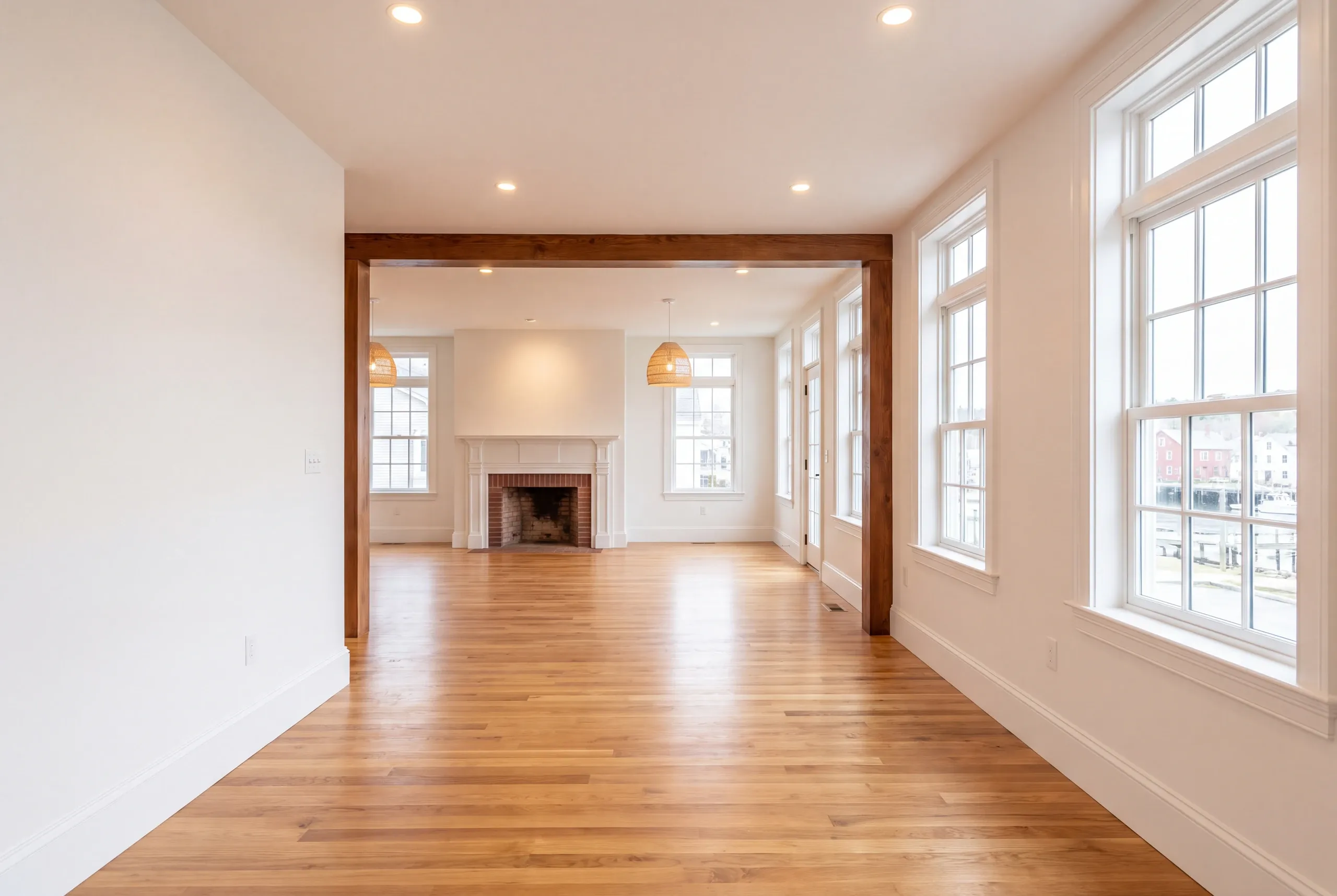 Remodeling company Belfast Maine: long room with a stained beam, a brick fireplace at the end and tall windows
