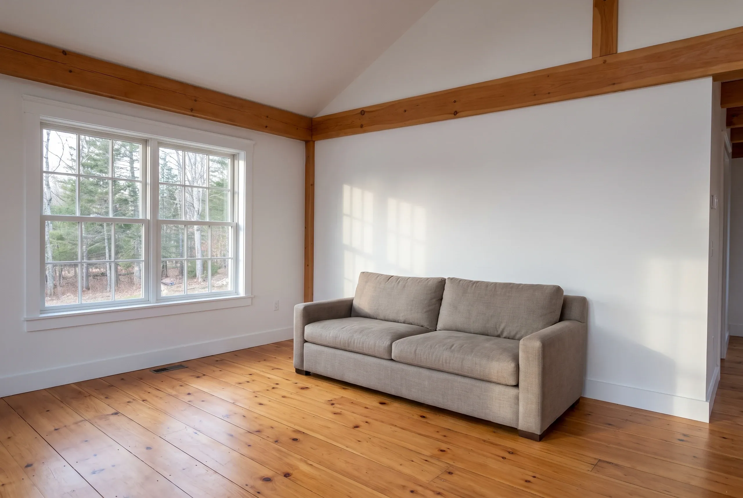Remodeling company Camden Maine: remodeled room with cathedral ceiling, exposed timber beam, wide window and refinished pine floor.