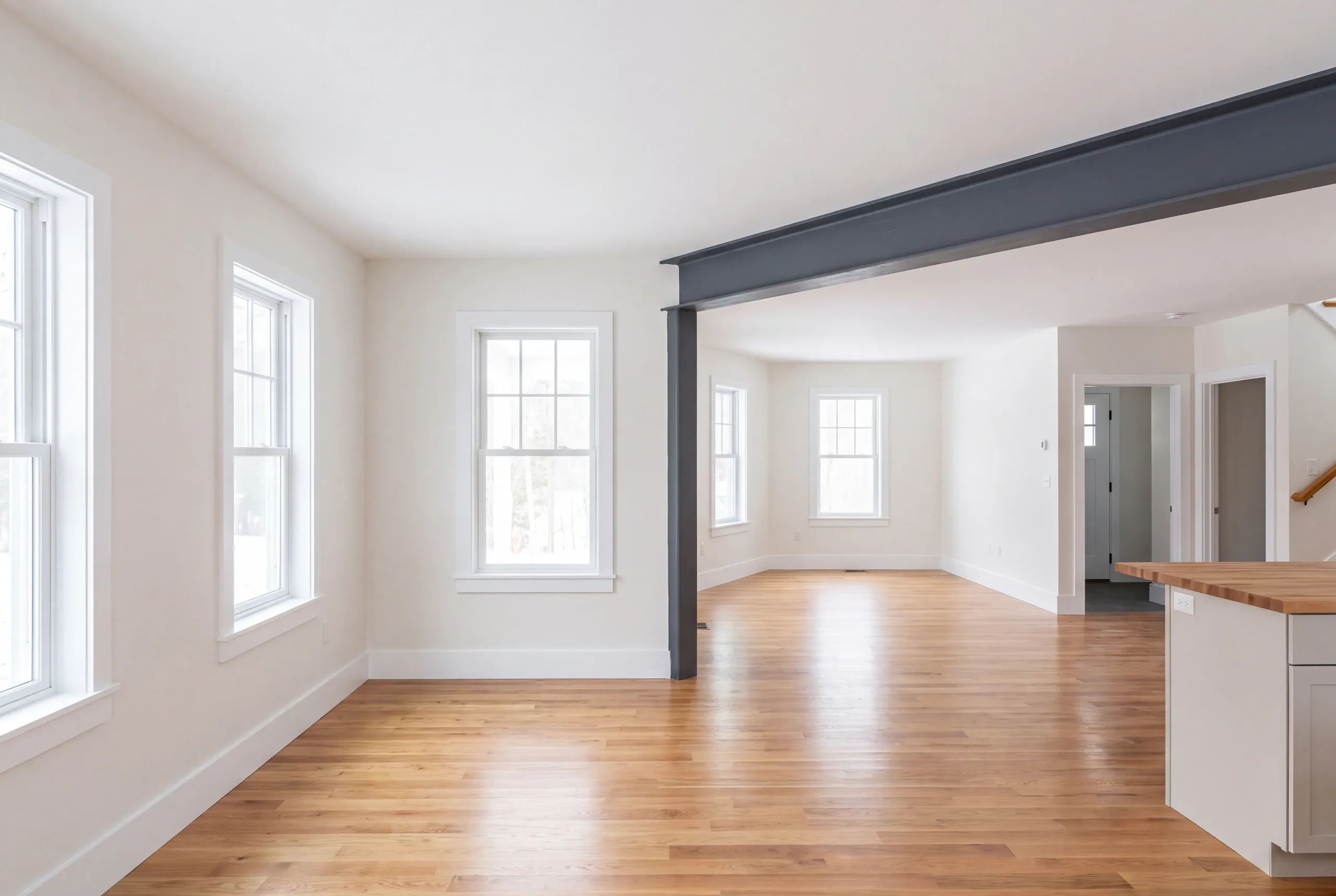 Home remodeling contractor Midcoast Maine: empty room with a black steel beam and post, oak floor and a kitchen island edge