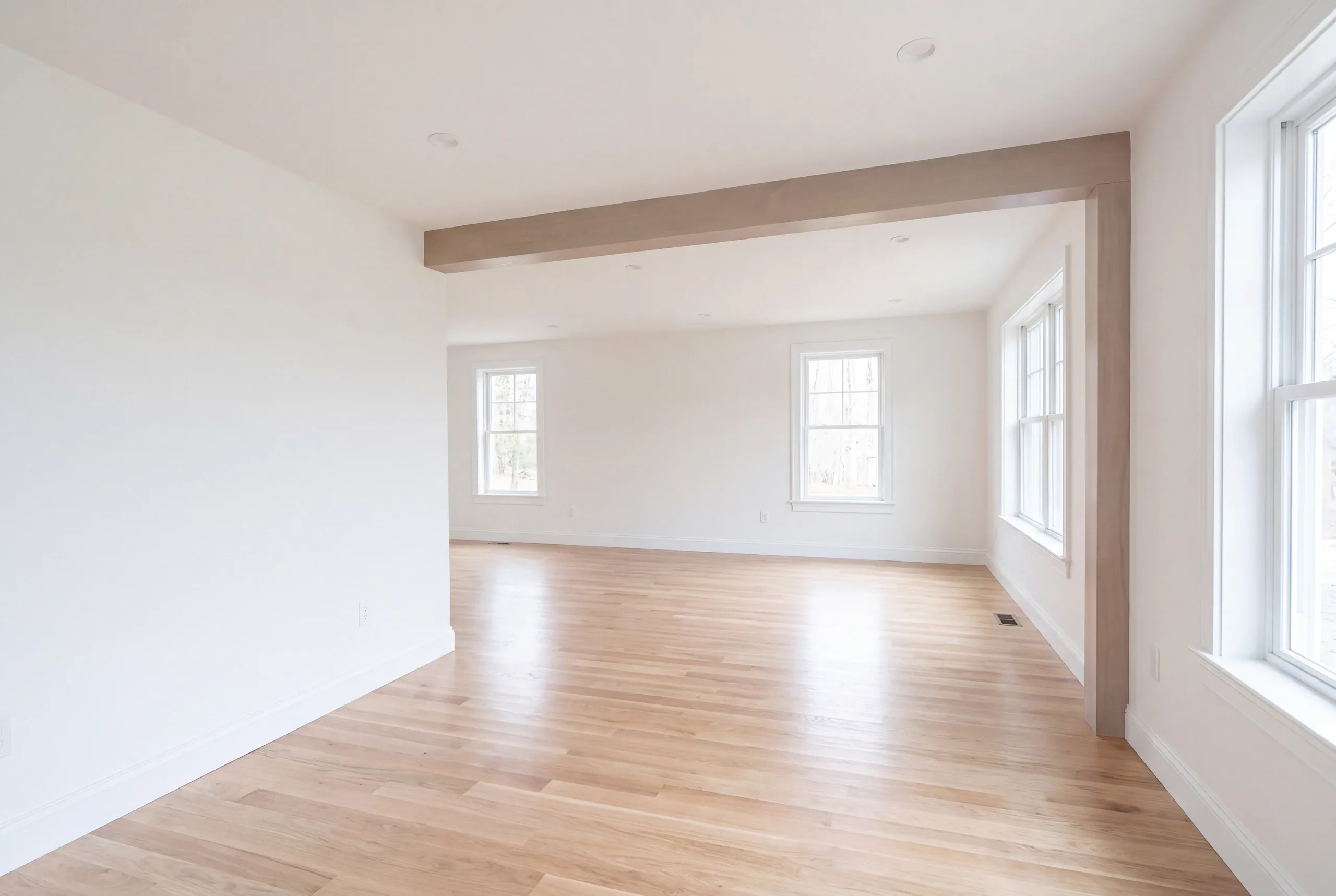Remodeling company Damariscotta Maine: empty room with a boxed beam, double-hung windows and light oak floor