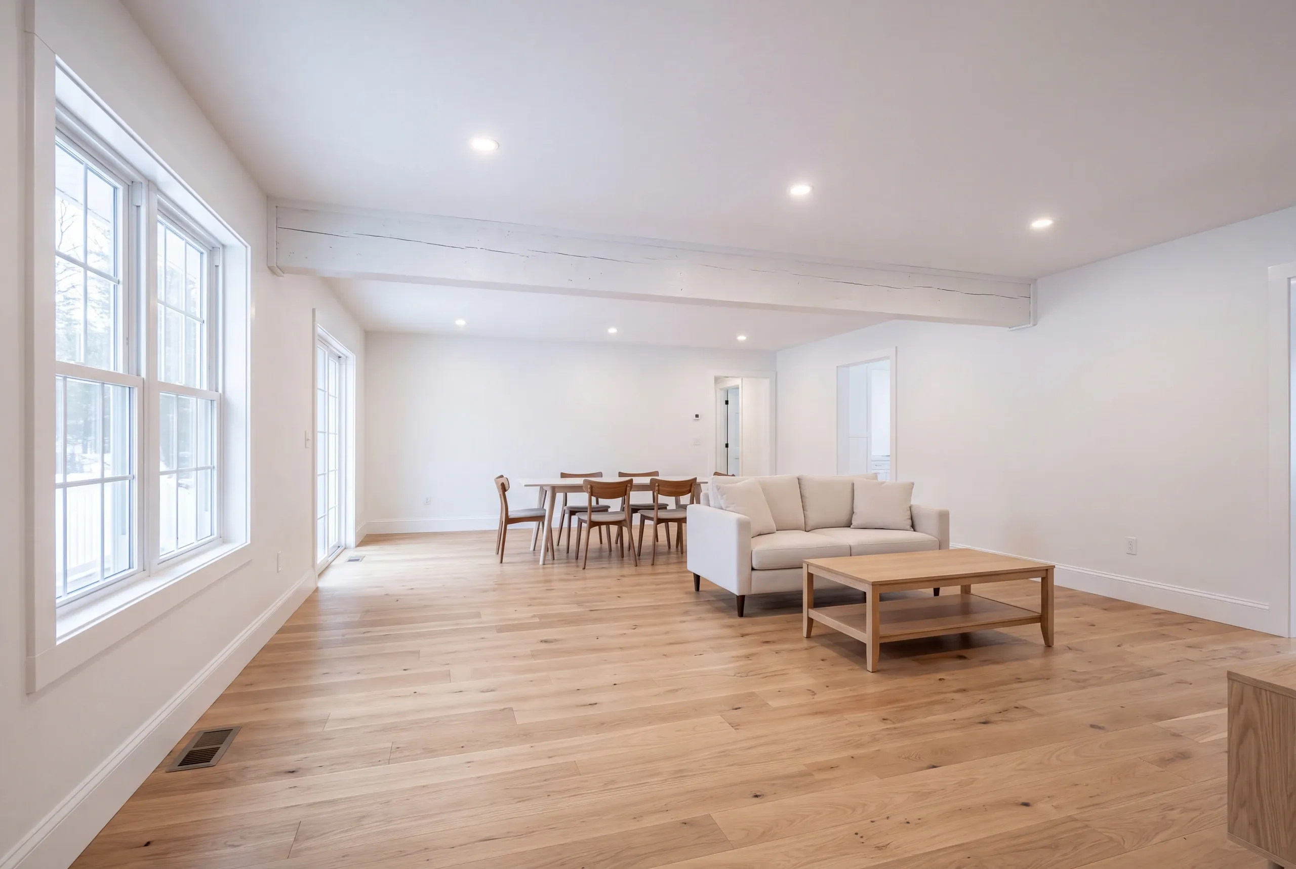 Home renovation contractor Fairfield Maine: open living and dining area with a white beam, linen sofa and oak coffee table