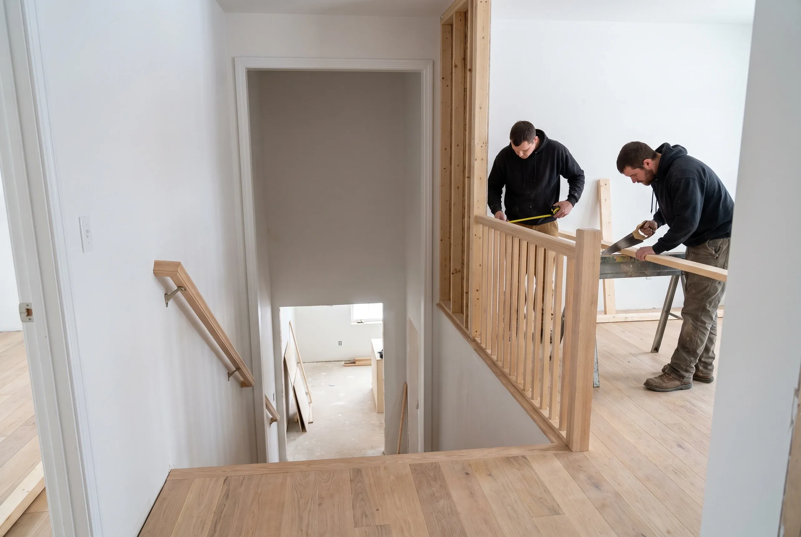 Home renovation contractor Gardiner Maine: crew fitting a new oak railing and balusters at the top of a stairwell with a handsaw