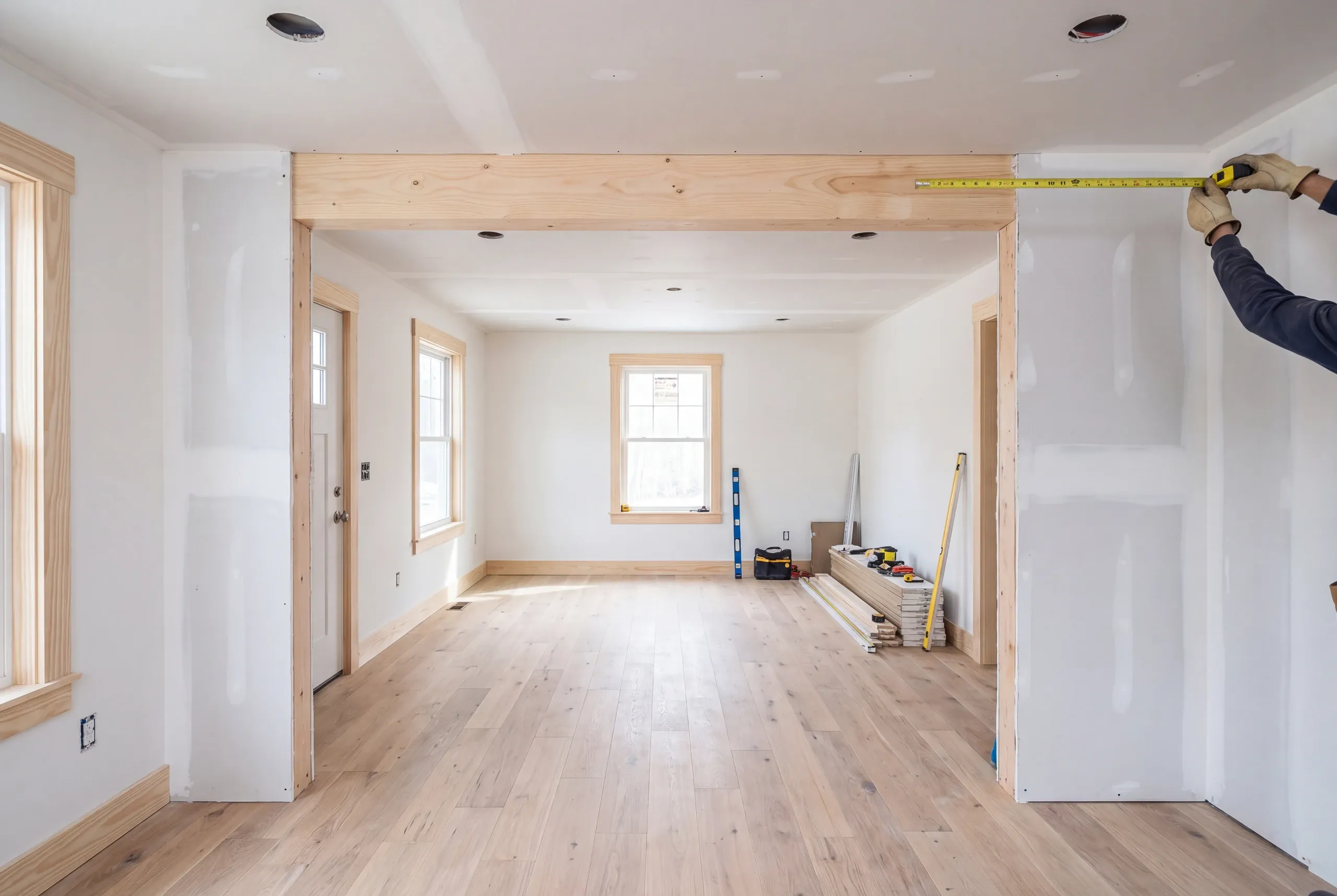 Home remodeling contractor Gardiner Maine: room mid-renovation with a new pine header, taped drywall and gloved hands measuring
