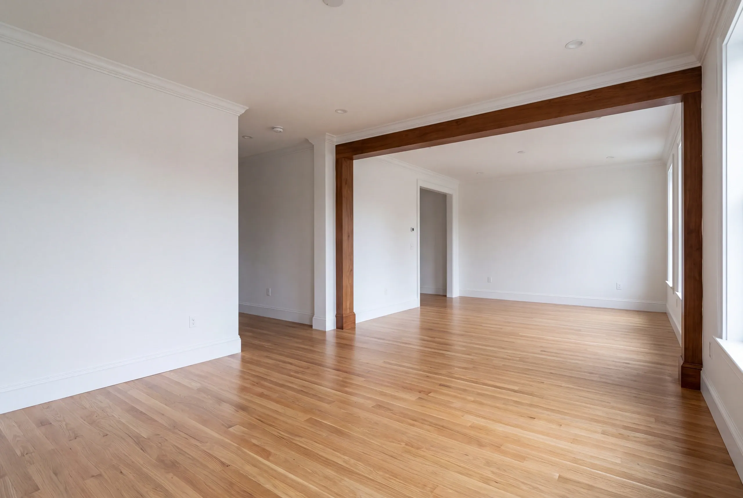 Home renovation contractor Gardiner Maine: empty room with a dark stained beam and post opening into a second room
