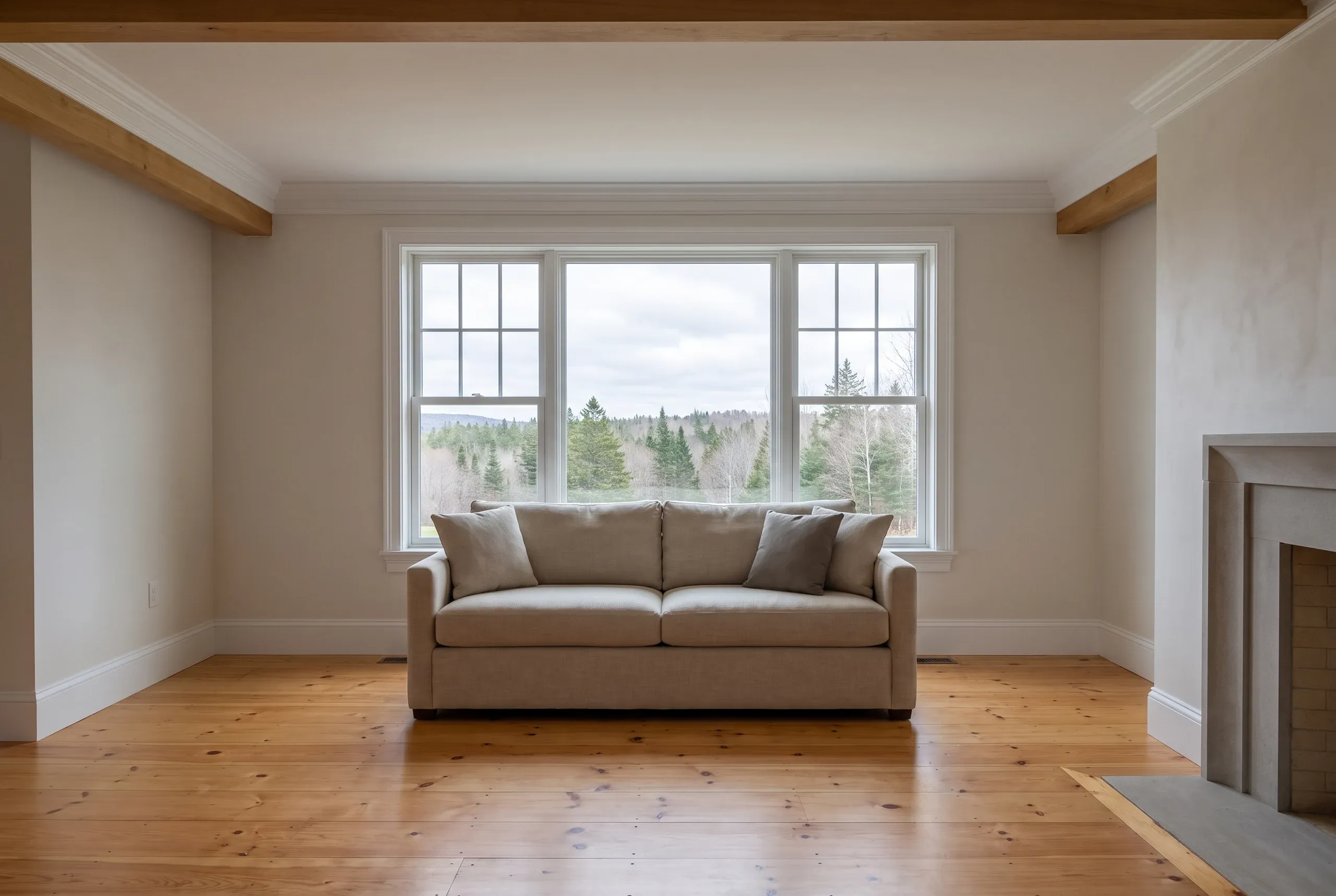 Home renovation contractor Lincolnville Maine: remodeled sitting room with exposed timber beams, large window and refinished wide-plank pine floor.