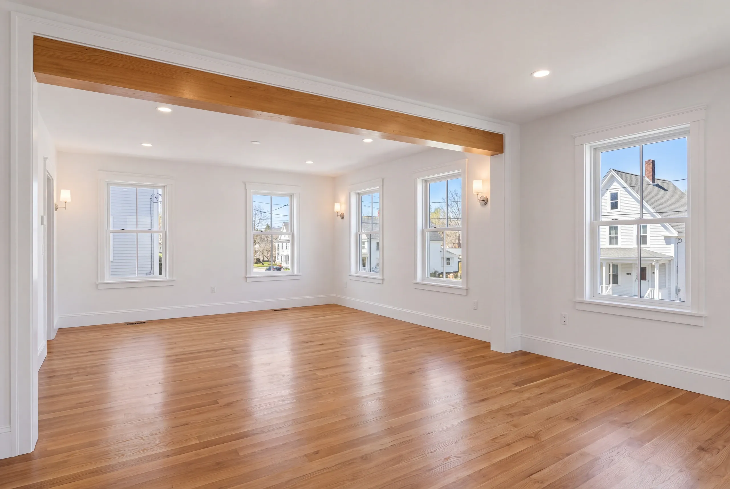 Home remodeling in Pittsfield, ME: empty room with a natural beam, wall sconces and windows onto a white house