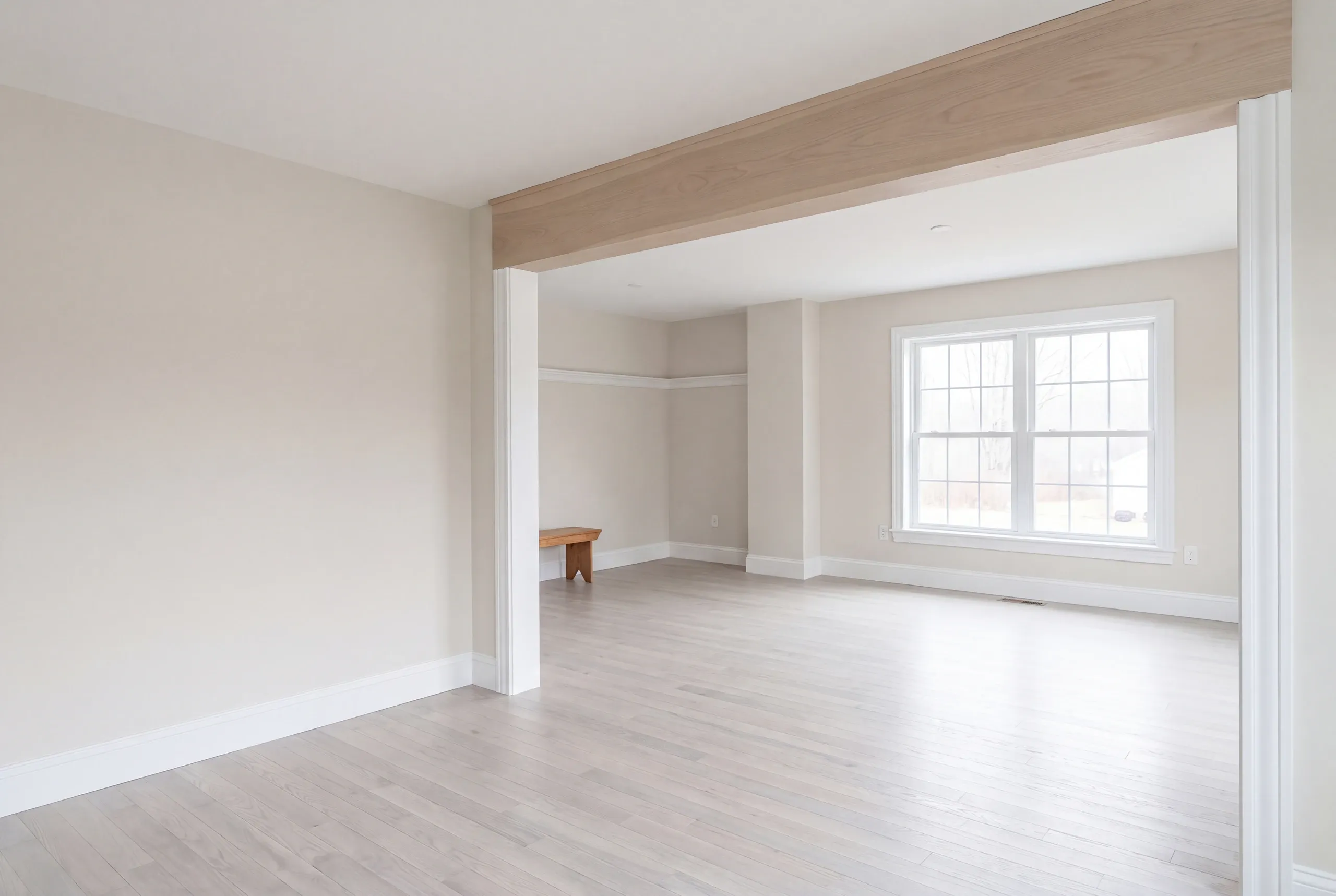 Remodeling company Pittsfield Maine: empty room with a pale beam over an opening, a small bench and gray-washed floor
