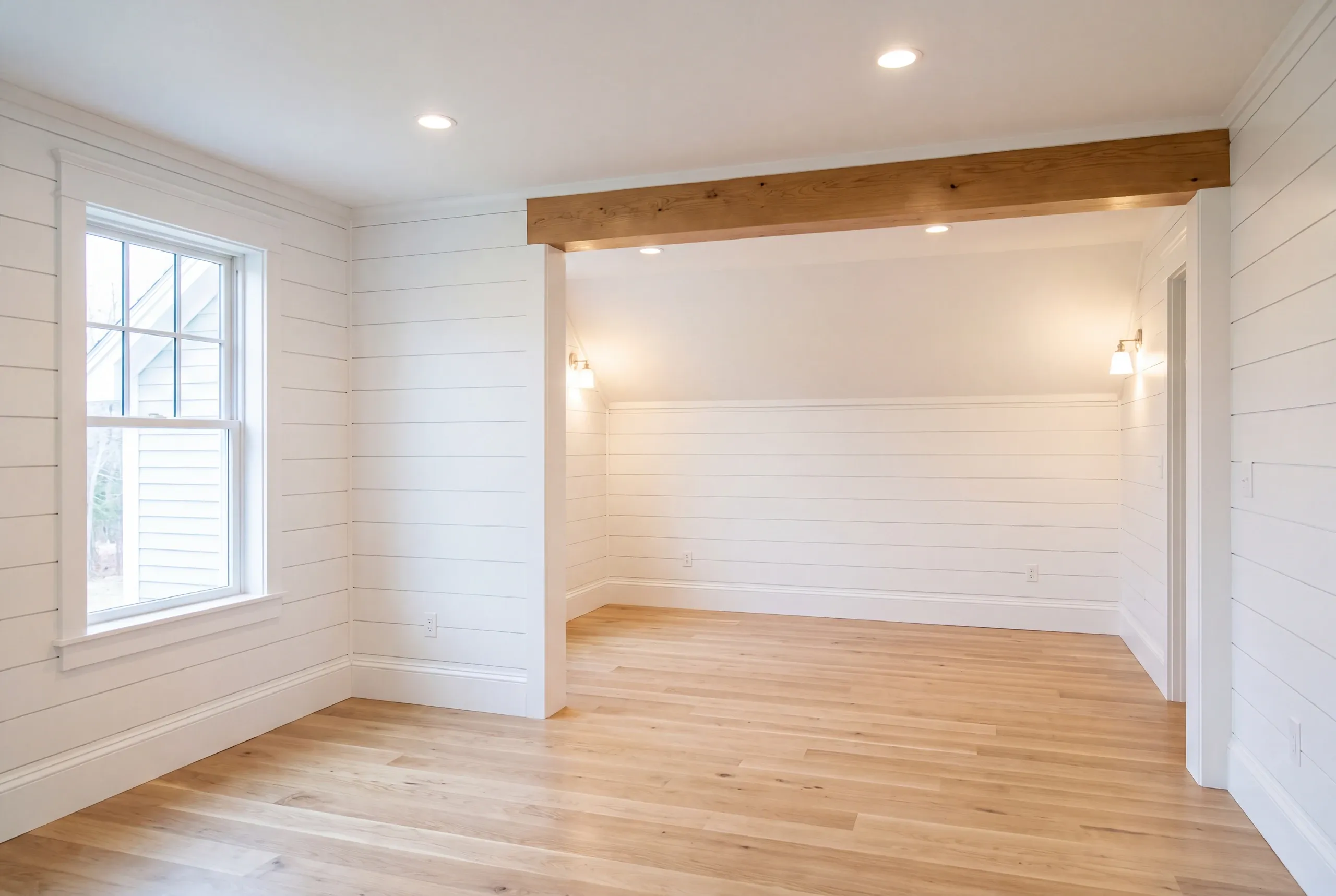 Home renovation contractor Pittston Maine: white shiplap room with a natural beam, wall sconces and wide oak floor
