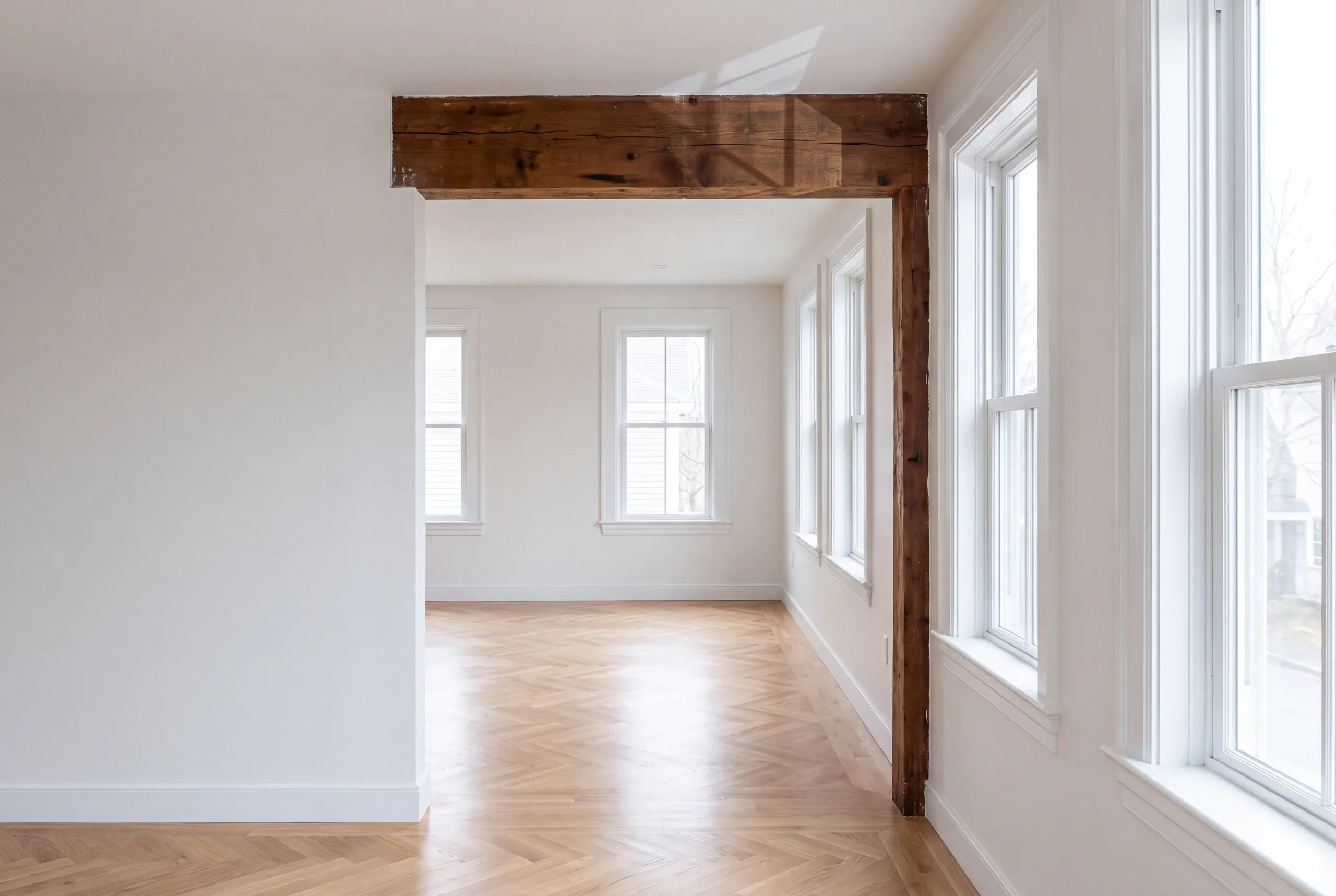 Remodeling company Rockland Maine: white room with a rough timber beam and post and herringbone-bordered oak floor