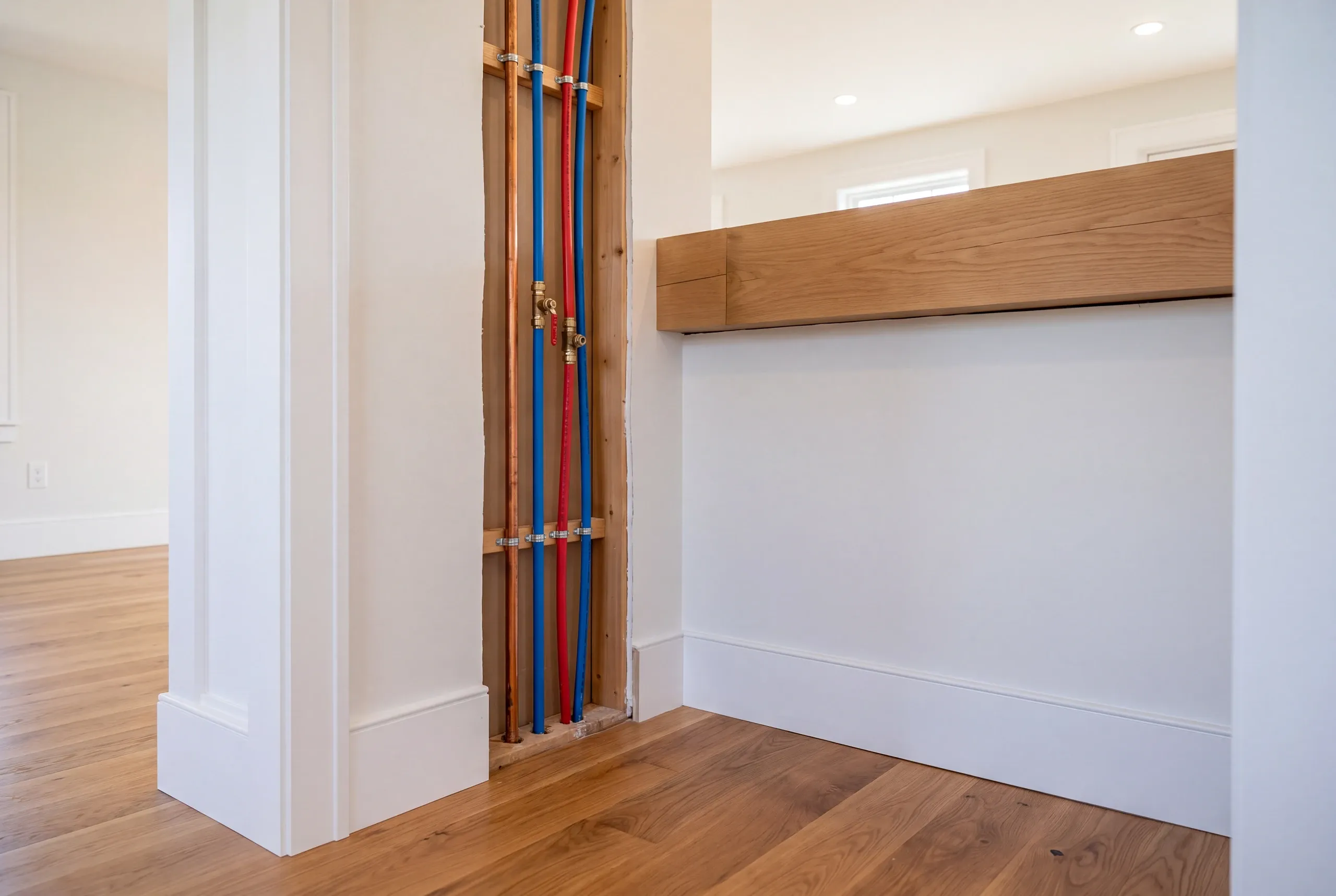 Home renovation contractor Rockport Maine: open wall chase with red and blue PEX lines beside finished trim and an oak beam