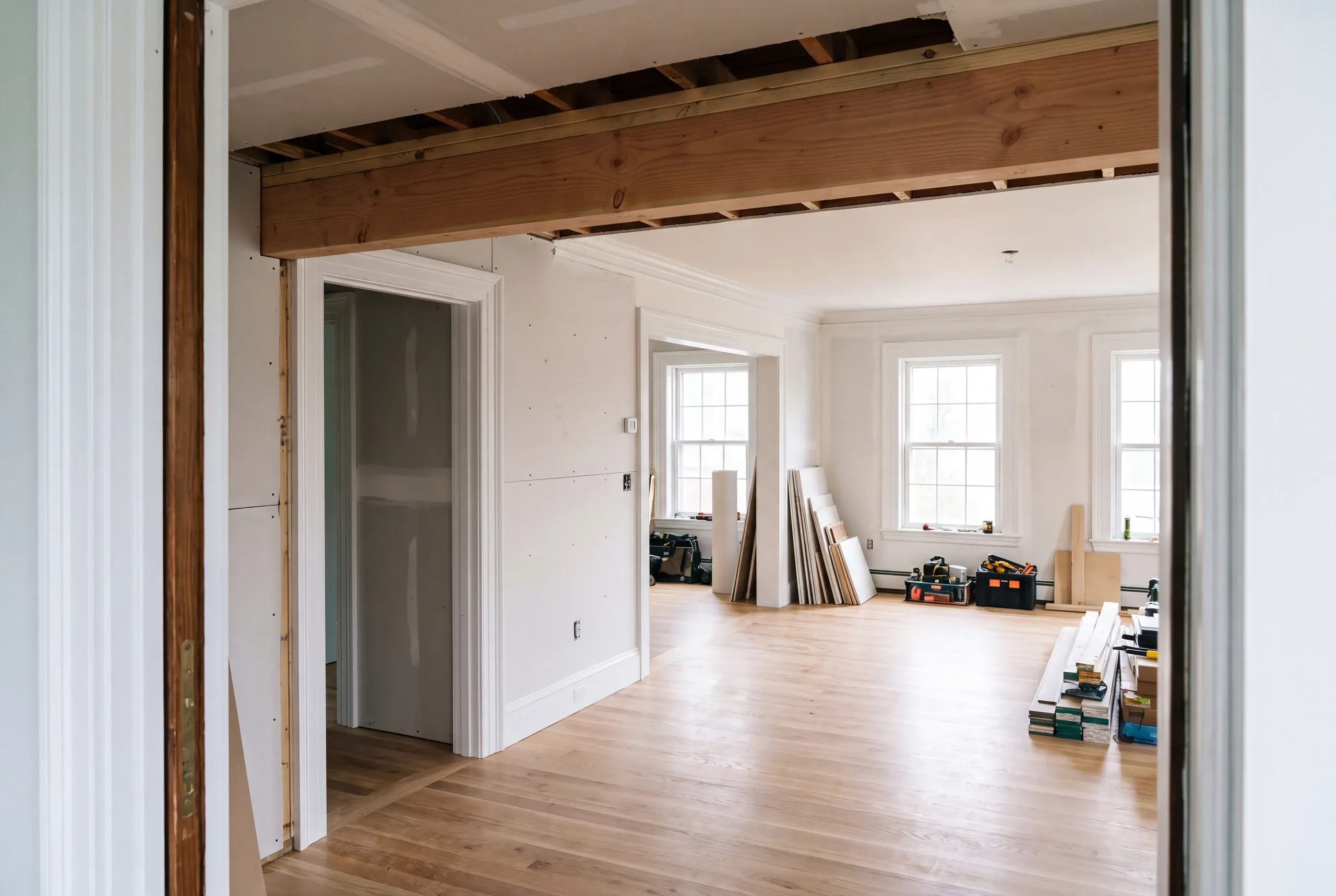Home remodeling contractor Rockport Maine: doorway view of a new beam under opened ceiling joists, drywall and tools beyond